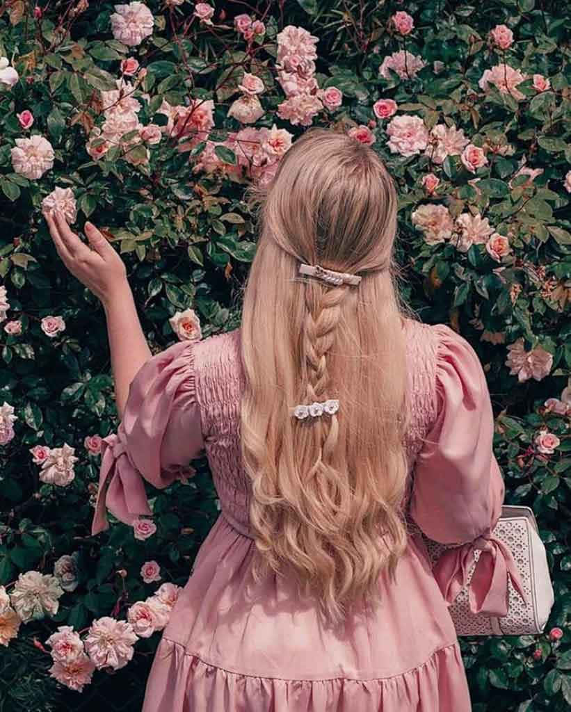 Pink Roses 桌布 壁紙 — 一位身穿粉紅色連衣裙、辮子頭髮的女性輕輕觸摸著開滿柔軟粉紅色花朵的玫瑰叢。