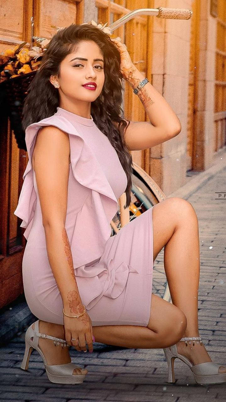 Nisha 桌布 壁紙 — 一位身穿粉紅色連衣裙的女性在鵝卵石街道上優雅地擺姿勢，旁邊是一輛復古自行車。