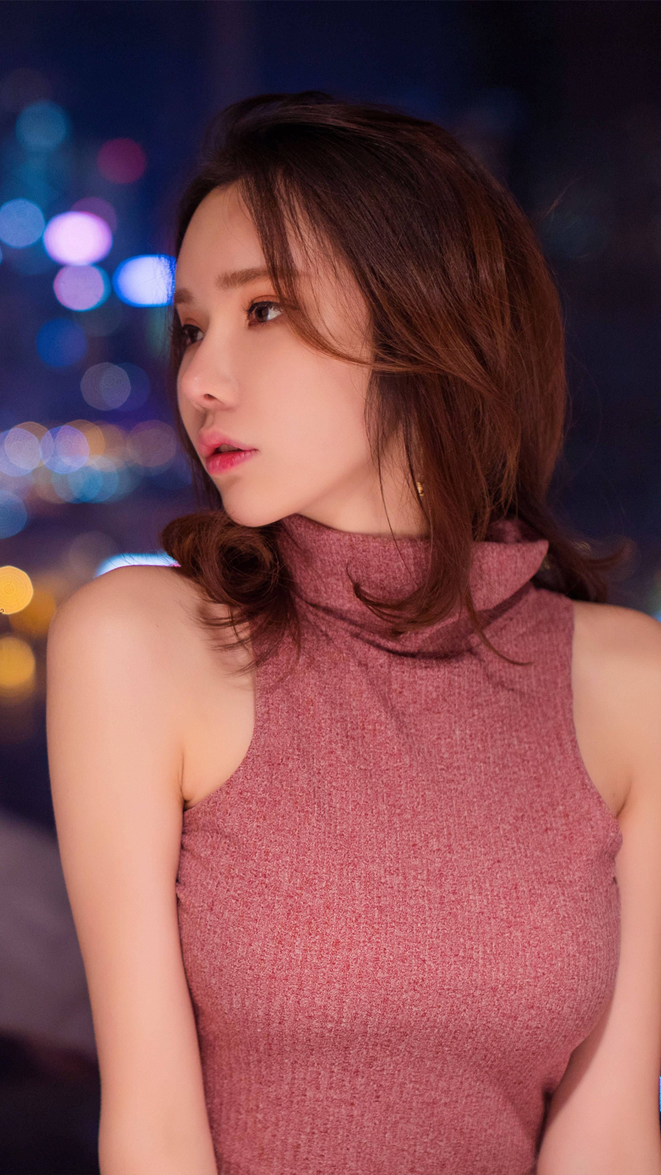 美女 桌布 壁紙 — 一位身穿粉紅色高領毛衣的女性，在充滿活力的散景城市夜景背景下若有所思地凝視。