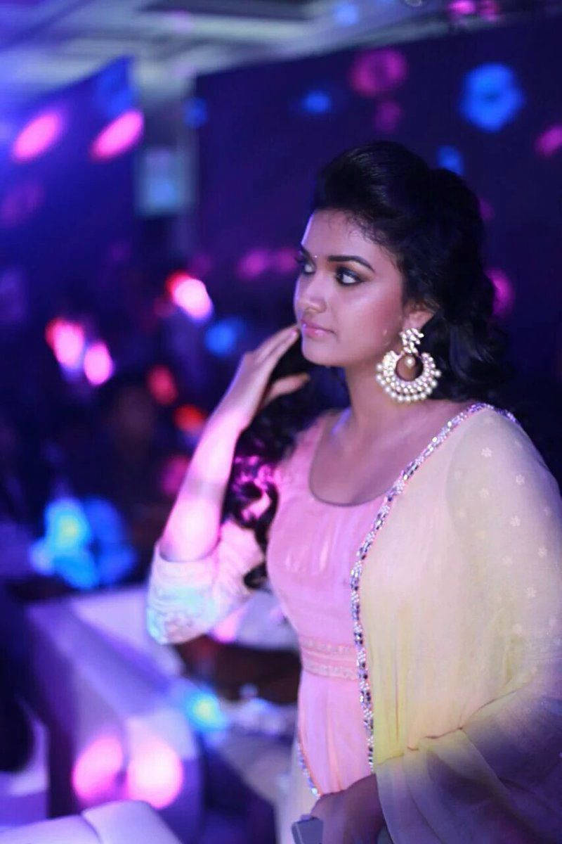 Keerthi Suresh HD 桌布 壁紙 — 一位身穿粉黃色傳統服飾的女性，在充滿活力的紫色和藍色迪斯科燈光下優雅地擺姿勢。