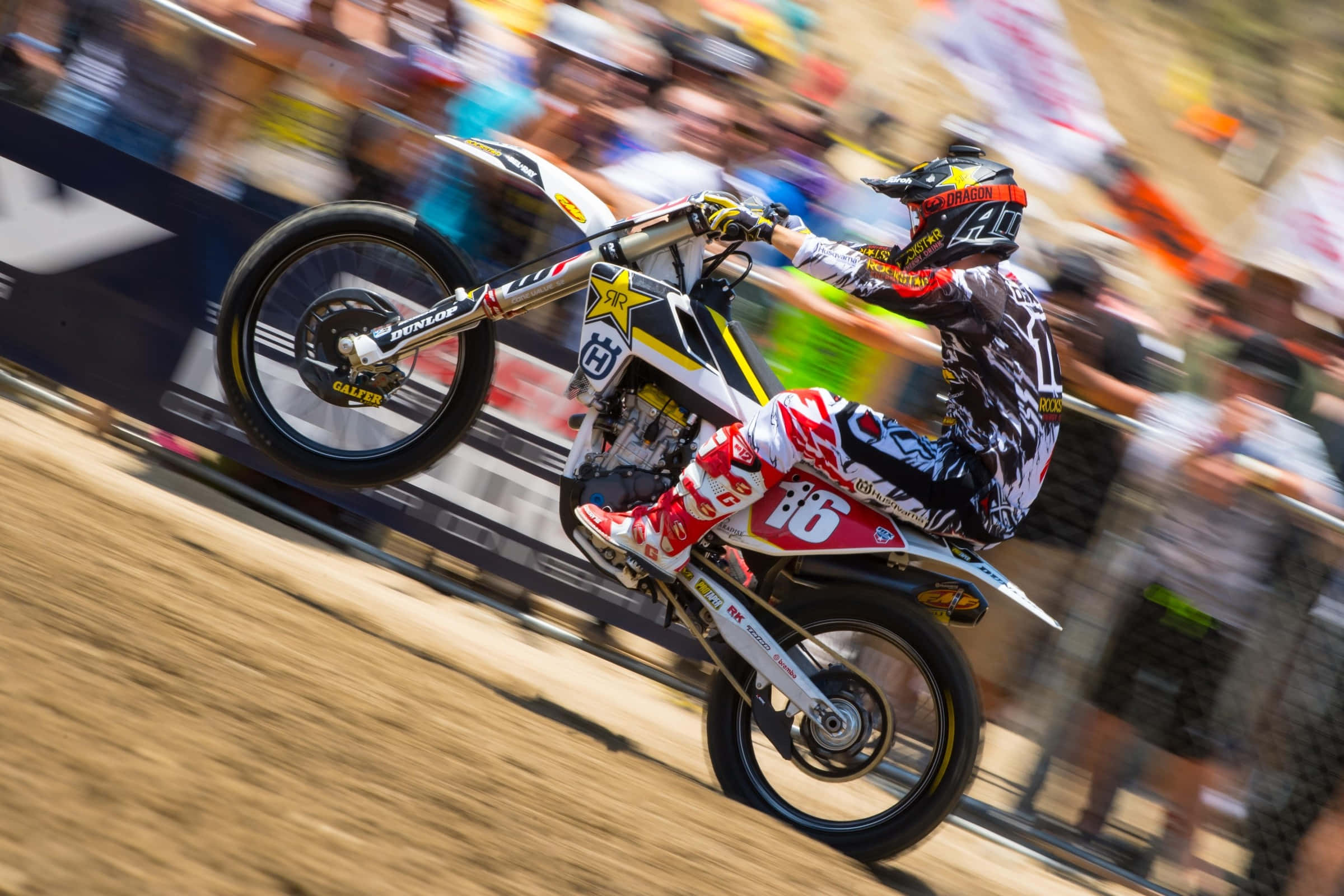 Motocross 桌布 壁紙 — 一位身穿紅、白、黑色裝備的越野摩托車手在泥地賽道上傾斜入彎，背景有模糊的觀眾。