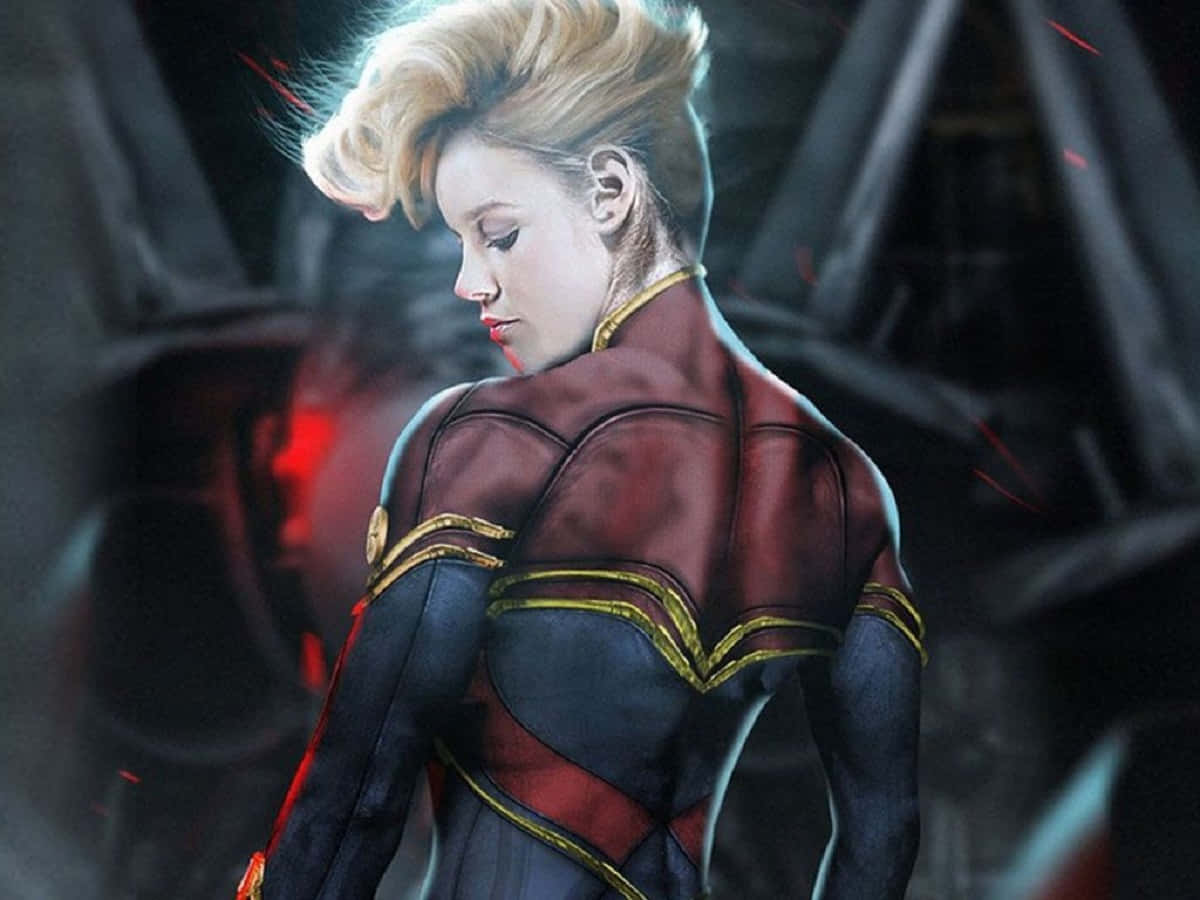 Captain Marvel 桌布 壁紙 — 一位身穿紅、藍、金色服裝的女性超級英雄站在黑暗的工業環境中，周圍有發光的紅色火花飛舞。