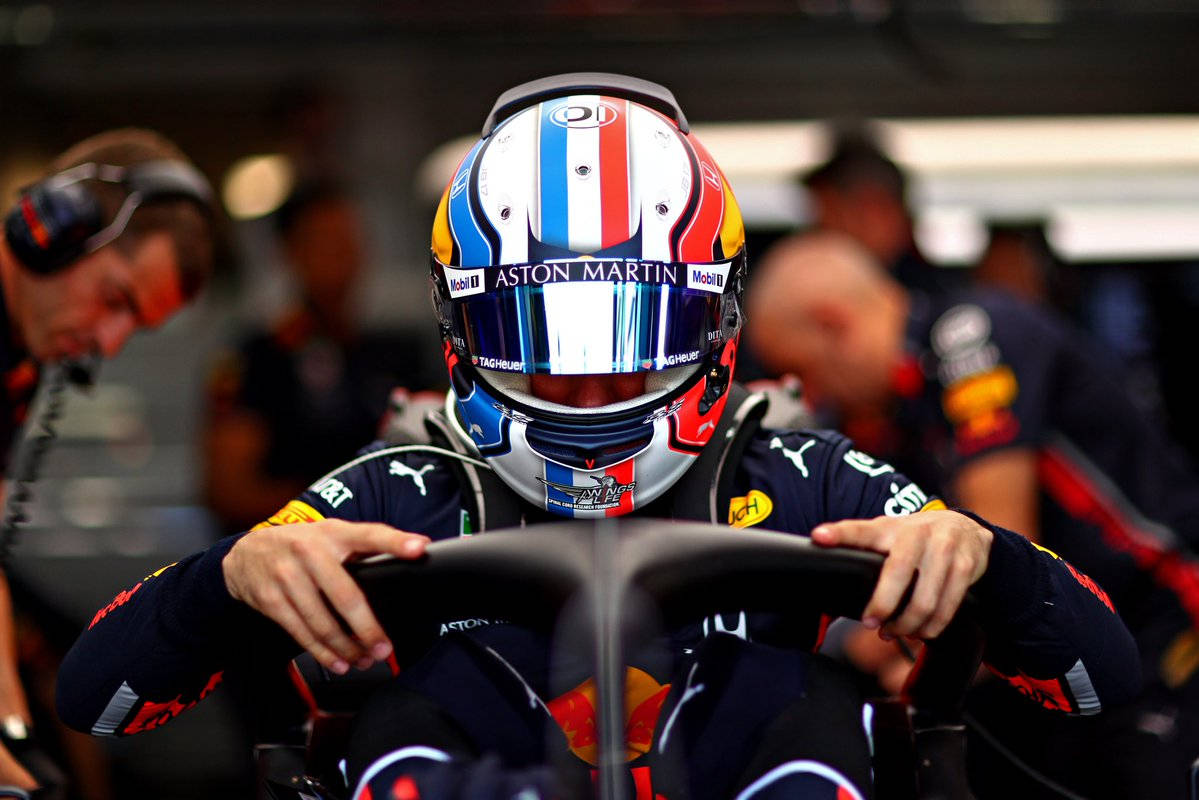 F1 桌布 壁紙 — 一位身穿紅牛車隊頭盔和賽車服的F1車手在車庫內握著賽車的方向盤。