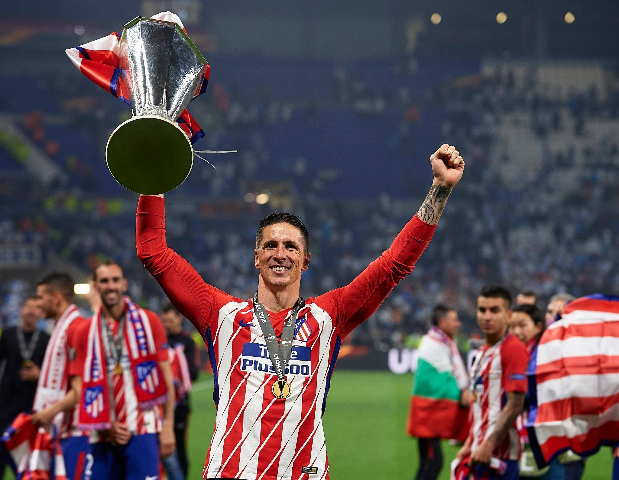 Torres 桌布 壁紙 — 一位身穿紅白條紋球衣的勝利足球員在球場上笑容滿面地將閃亮的銀色獎盃高舉過頭。