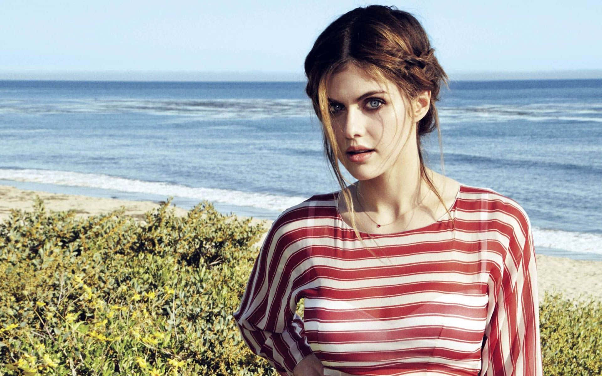 Alexandra Daddario 桌布 壁紙 — 一位身穿紅白條紋襯衫的女性站在海邊，身後有海浪拍打。