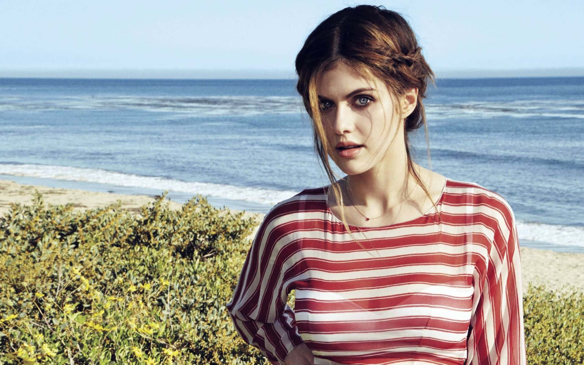 Alexandra Daddario 桌布 壁紙 — 一位身穿紅白條紋襯衫的女性站在海邊，身後波濤洶湧。