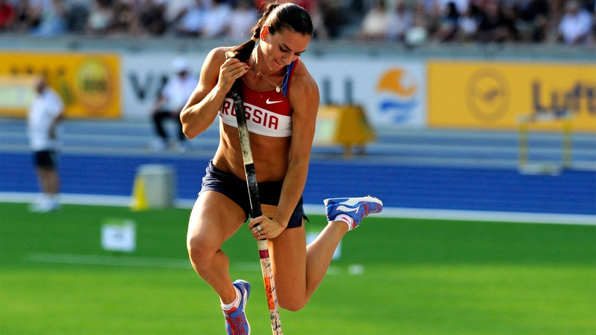 Athletic 桌布 壁紙 — 一位身穿紅白藍裝備的俄羅斯女子撐竿跳運動員，在明亮的日光下於綠色跑道上準備跳躍。