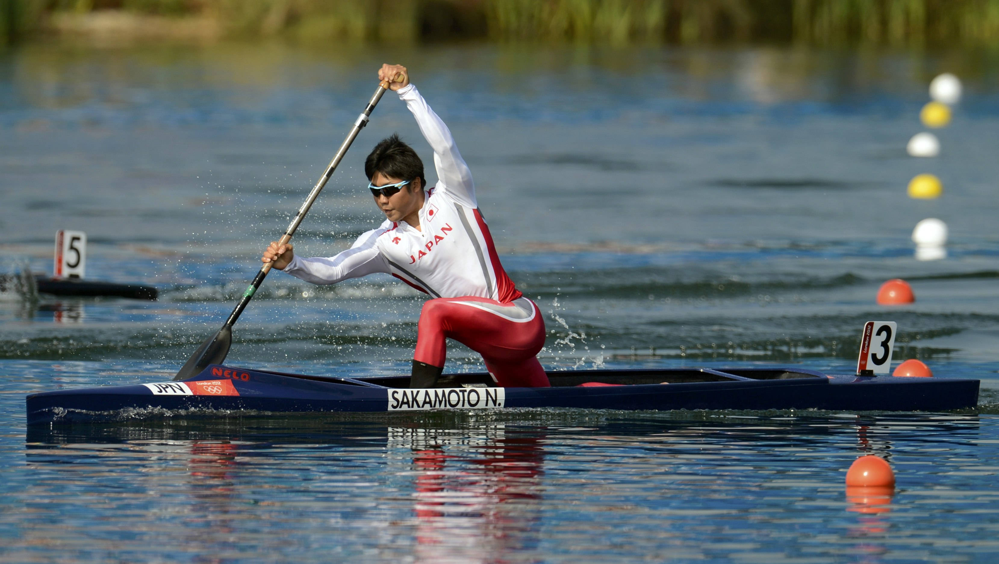 Rowing 桌布 壁紙 — 一位身穿紅白裝備的日本皮划艇選手在平靜的藍色水面上以專注的強度奮力划行，進行一場競技比賽。