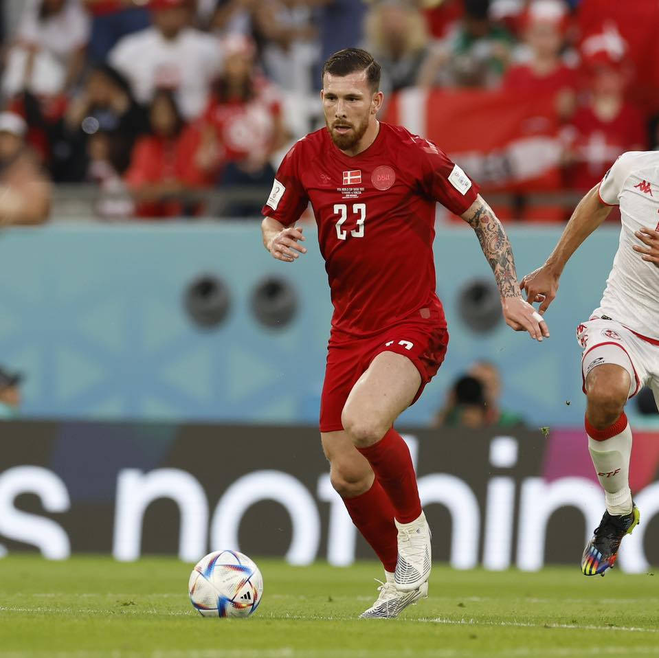 Football Players 桌布 壁紙 — 一位身穿紅色23號球衣的丹麥足球員在球場燈光下專注地運球。