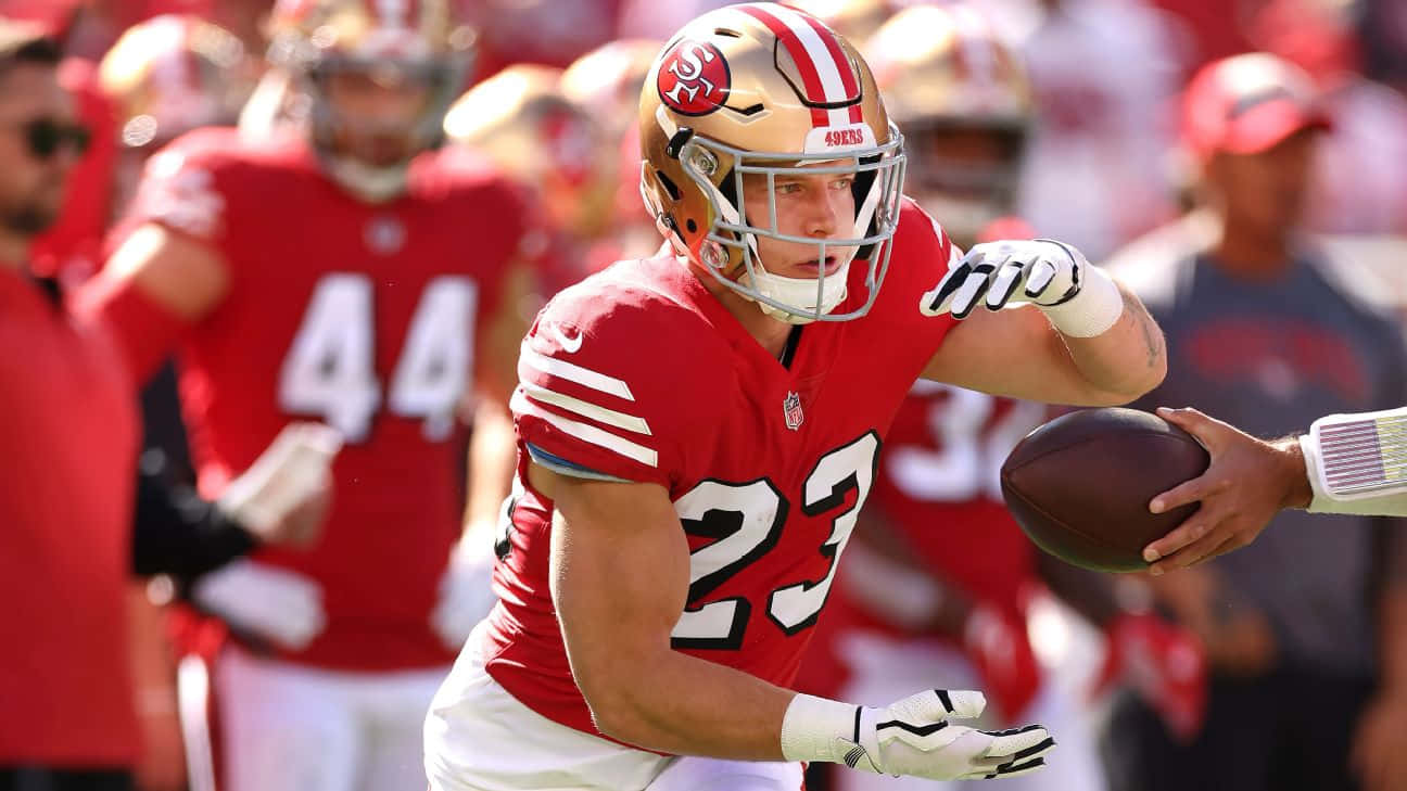 Christian Mccaffrey 桌布 壁紙 — 一位身穿紅色23號球衣的舊金山四九人美式足球員，在陽光明媚的日間比賽中準備擲球。