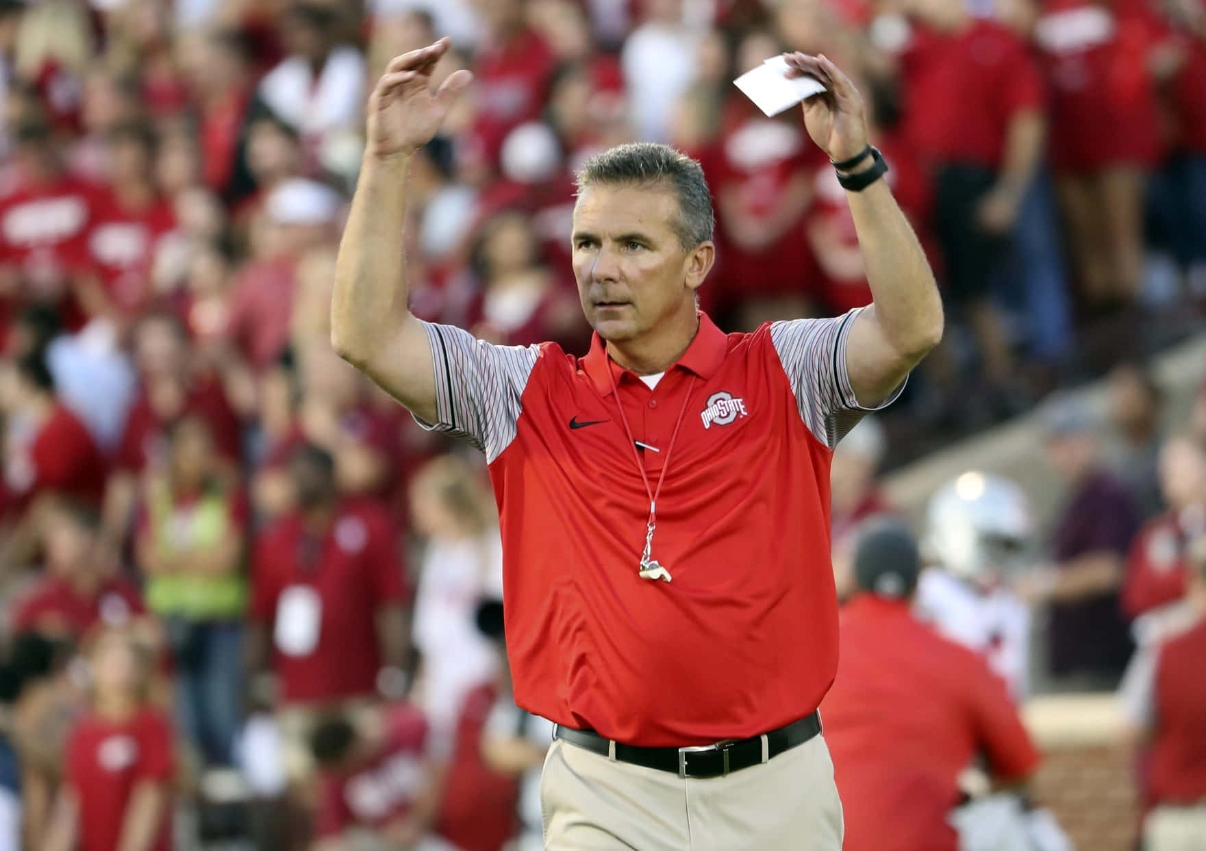 Urban Meyer 桌布 壁紙 — 一位身穿紅色Polo衫的足球教練在比賽期間在邊線舉起白牌並用力做手勢。