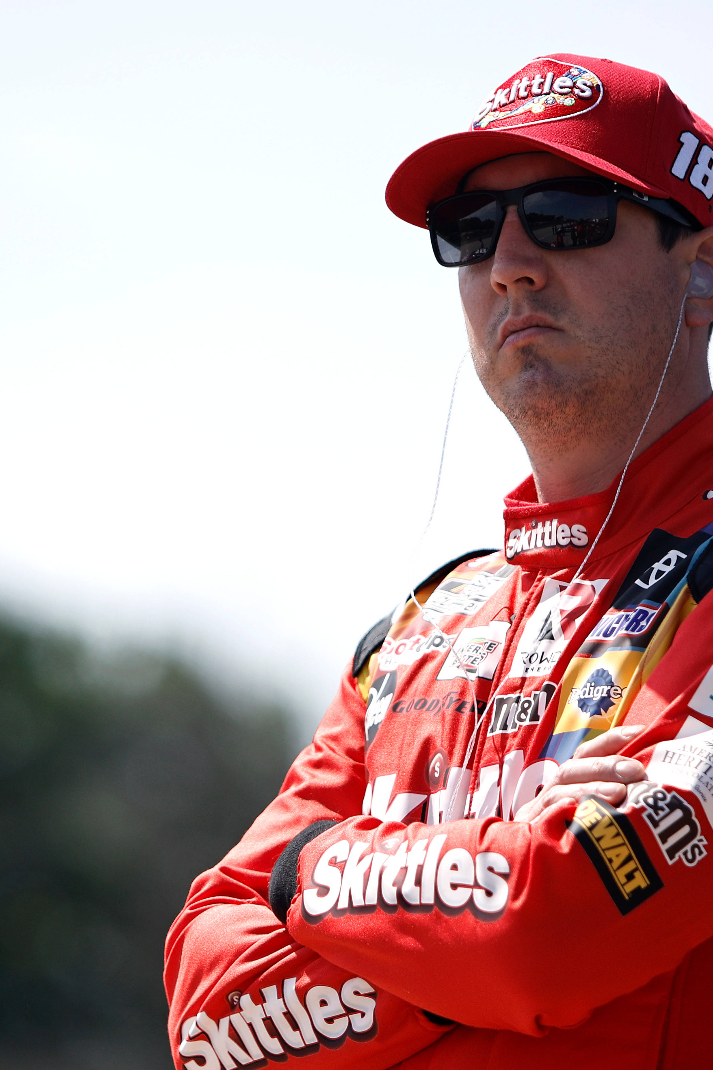 Racing 桌布 壁紙 — 一位身穿紅色Skittles賽車服和帽子的NASCAR車手在明亮的日光下交叉雙臂站立。