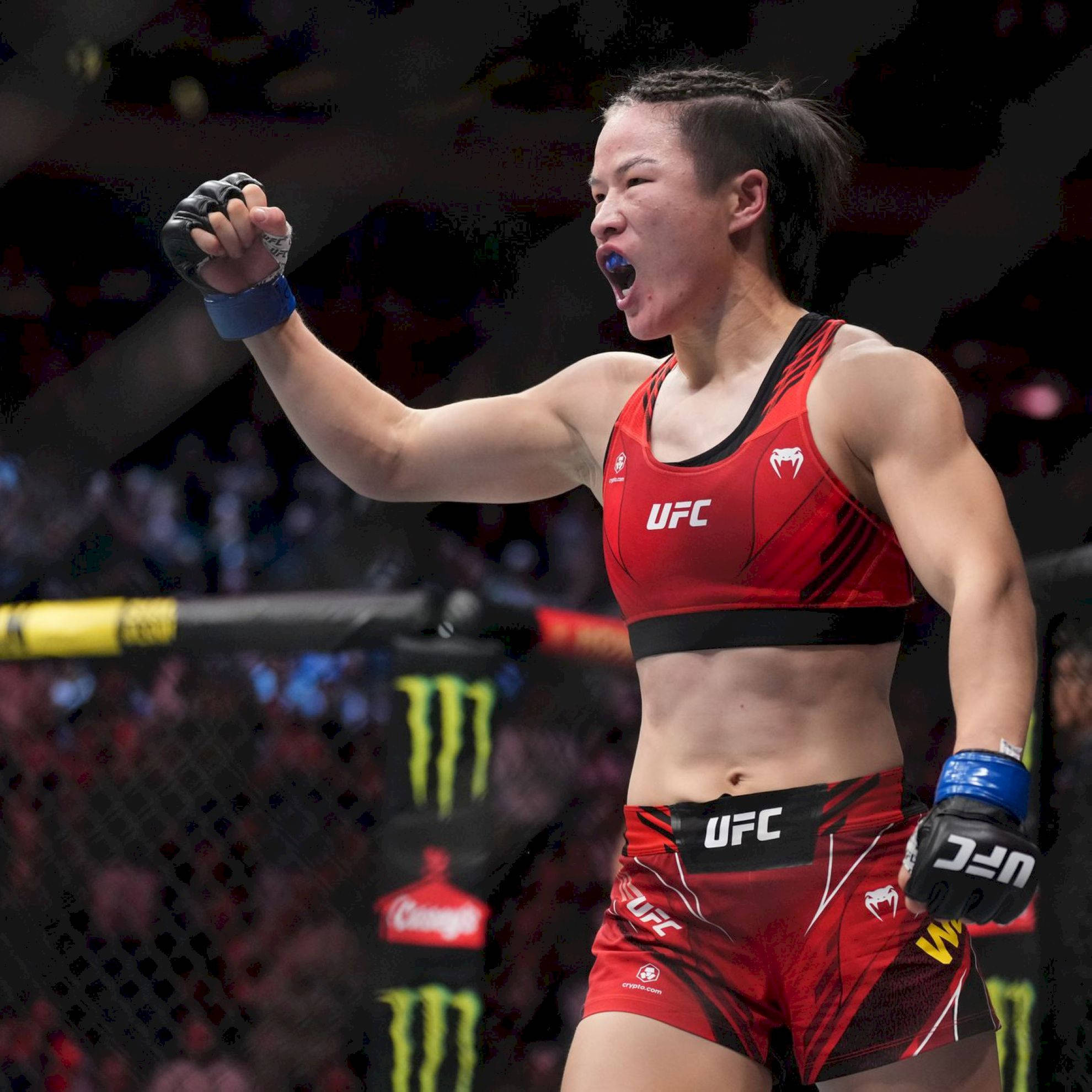 Champion 桌布 壁紙 — 一位身穿紅色UFC裝備的女性MMA拳手在明亮的場館燈光下，在籠內高舉拳頭勝利咆哮。
