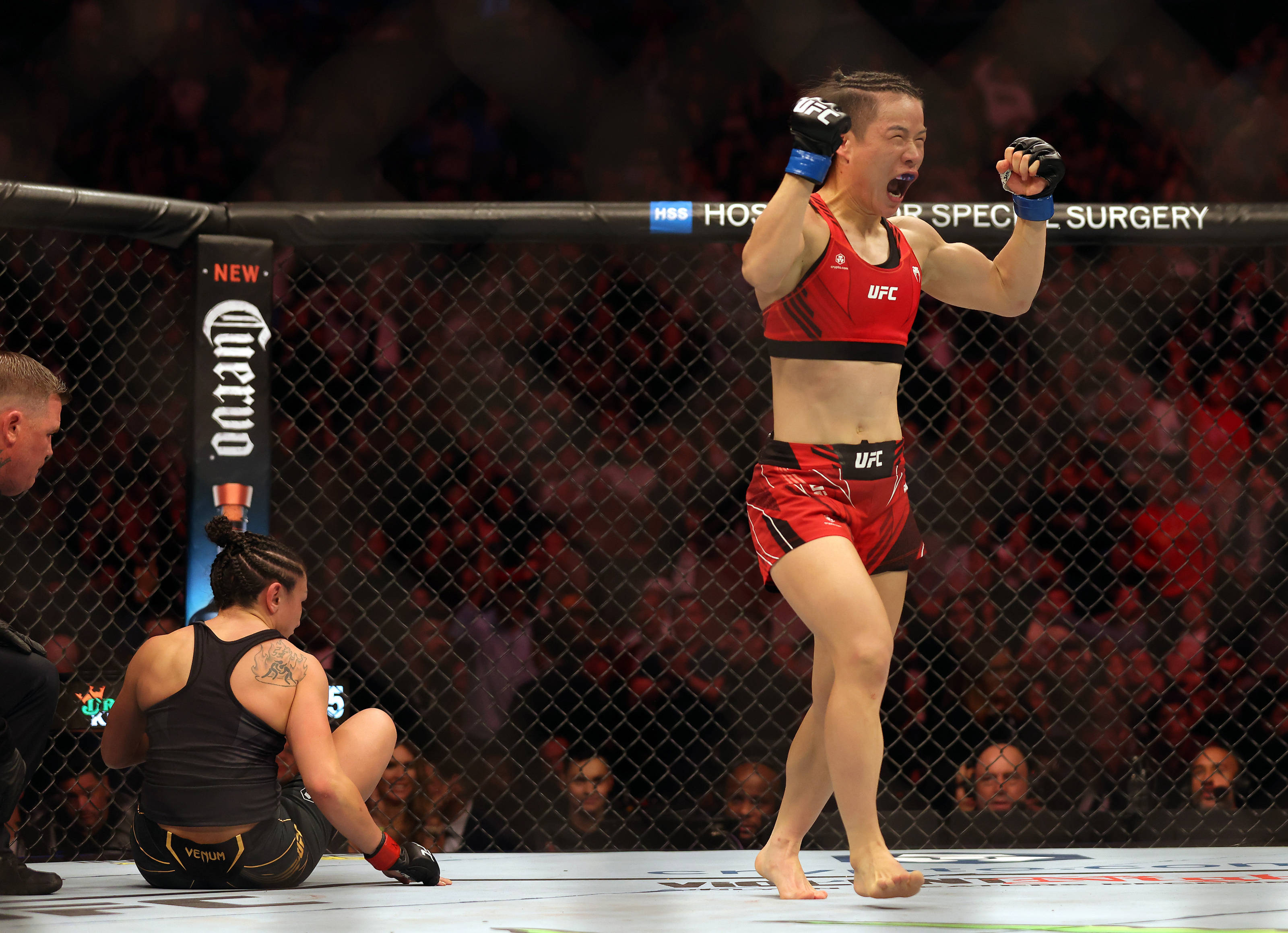 運動 桌布 壁紙 — 一位身穿紅色UFC裝備的女性MMA拳手在八角籠中慶祝勝利，而她的對手則坐在地上被擊敗。