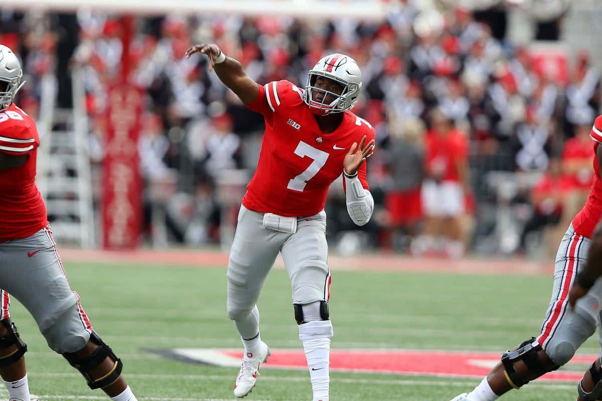 Dwayne Haskins 桌布 壁紙 — 一位身穿紅色七號球衣的美式足球四分衛在日間比賽中傳球，背景有模糊的球迷。