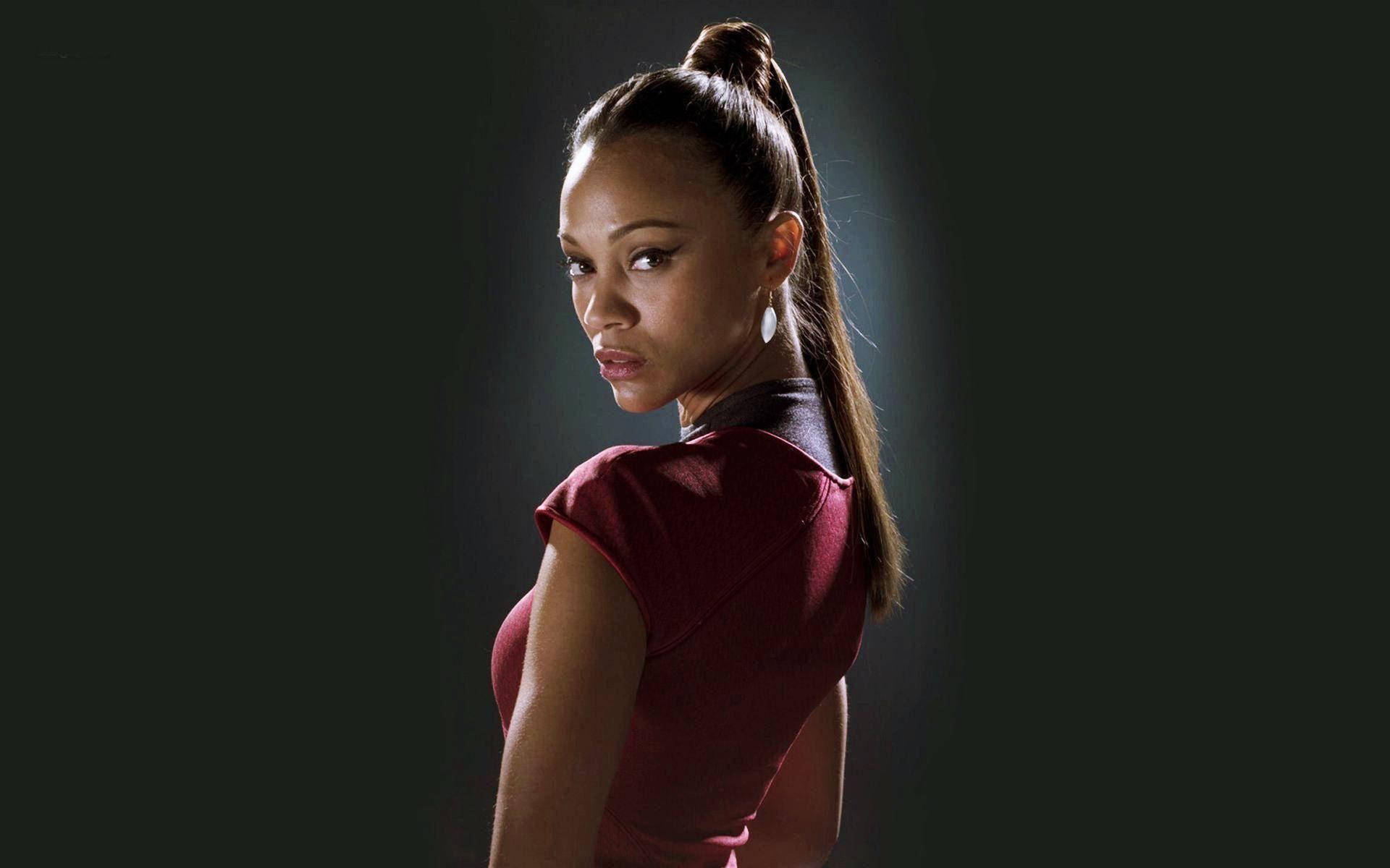 Zoe Saldana 桌布 壁紙 — 一位身穿紅色上衣的女性在黑暗背景中，戲劇性燈光下轉頭越過肩膀。