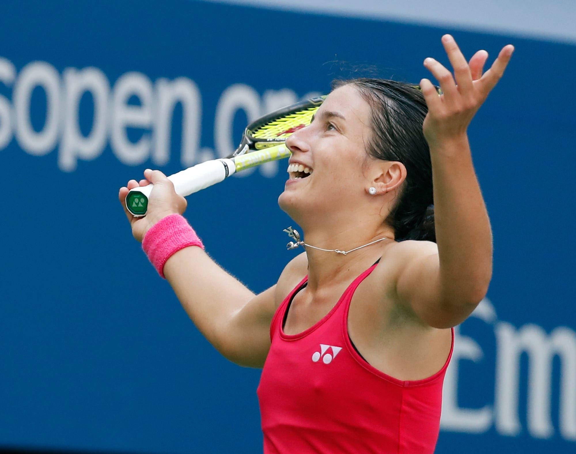 Tennis 桌布 壁紙 — 一位身穿紅色上衣的快樂女網球選手在藍色球場背景下高舉球拍慶祝勝利。