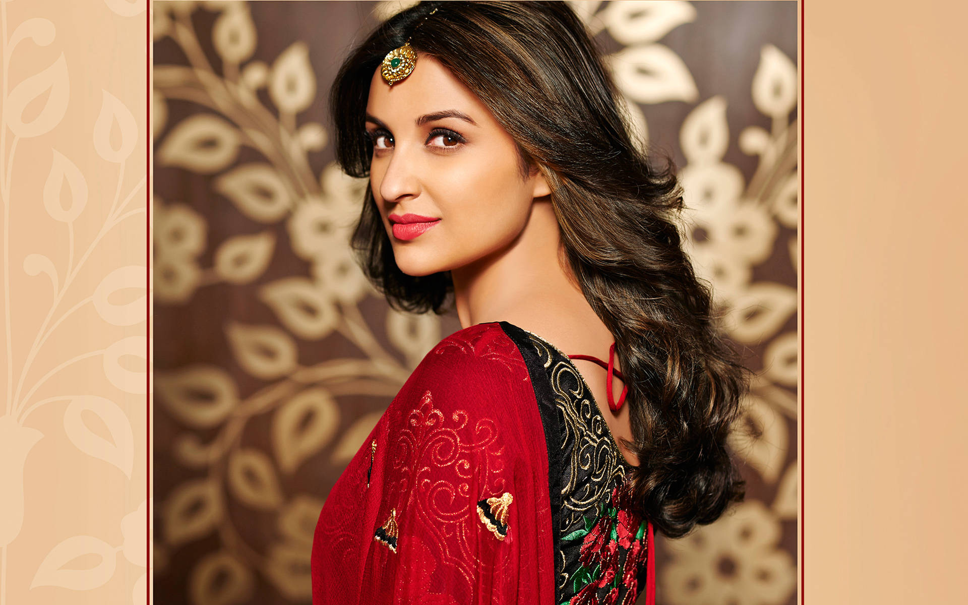 Parineeti 桌布 壁紙 — 一位身穿紅色刺繡服飾、頭戴金色頭飾的女性，在棕色和米色圖案背景前擺姿勢。