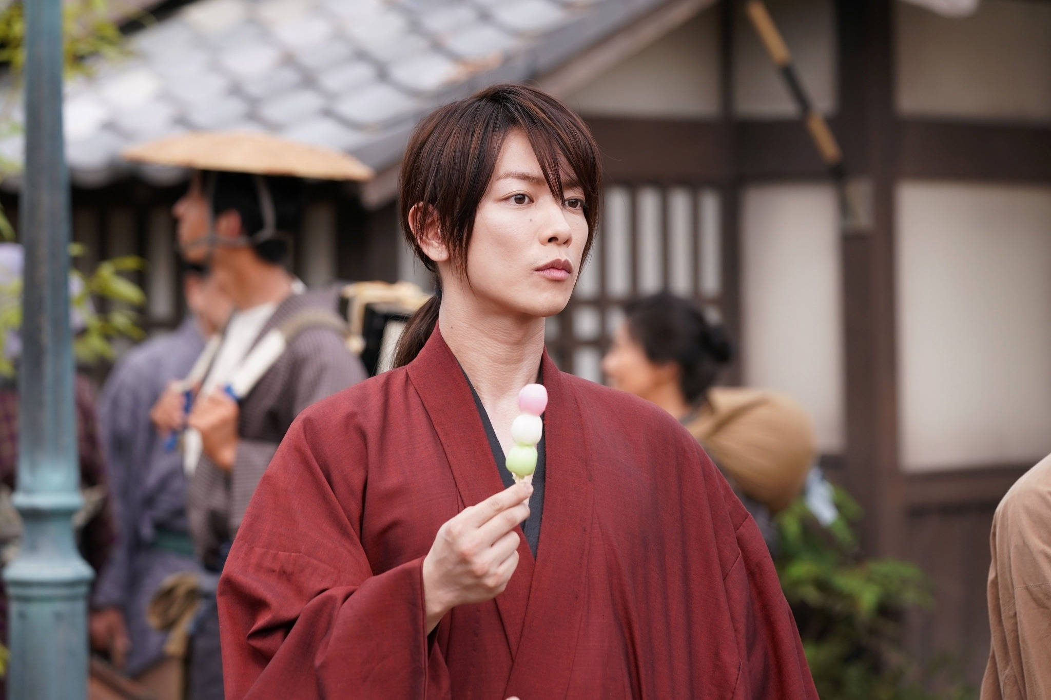 Kenshin 桌布 壁紙 — 一位身穿紅色和服的年輕男子，在傳統日本街景中手持一串色彩繽紛的糰子。