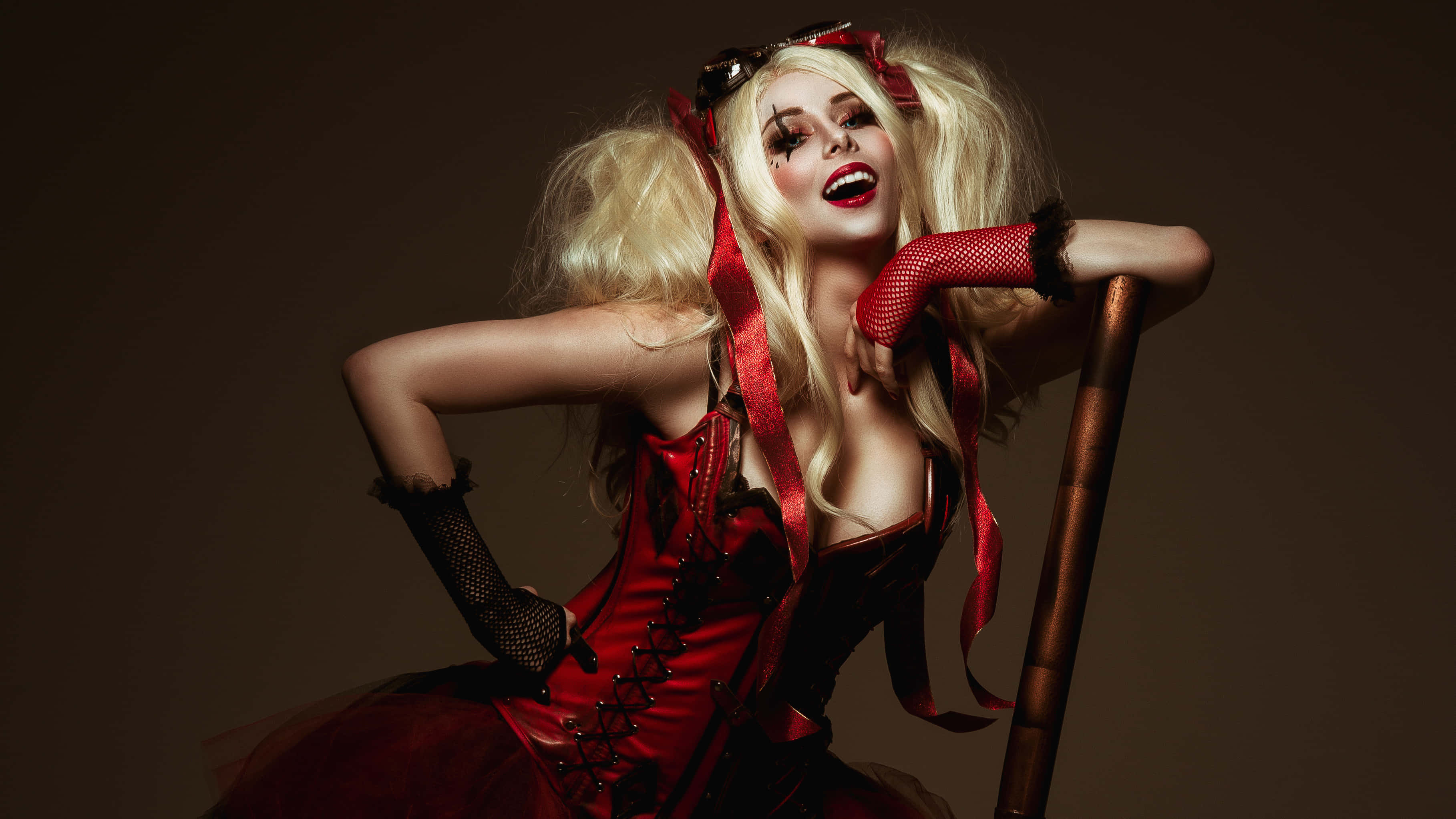 Harley Quinn Cosplay 桌布 壁紙 — 一位身穿紅色哈莉·奎茵服裝的女性在深棕色背景前自信地坐在木椅上擺姿勢。
