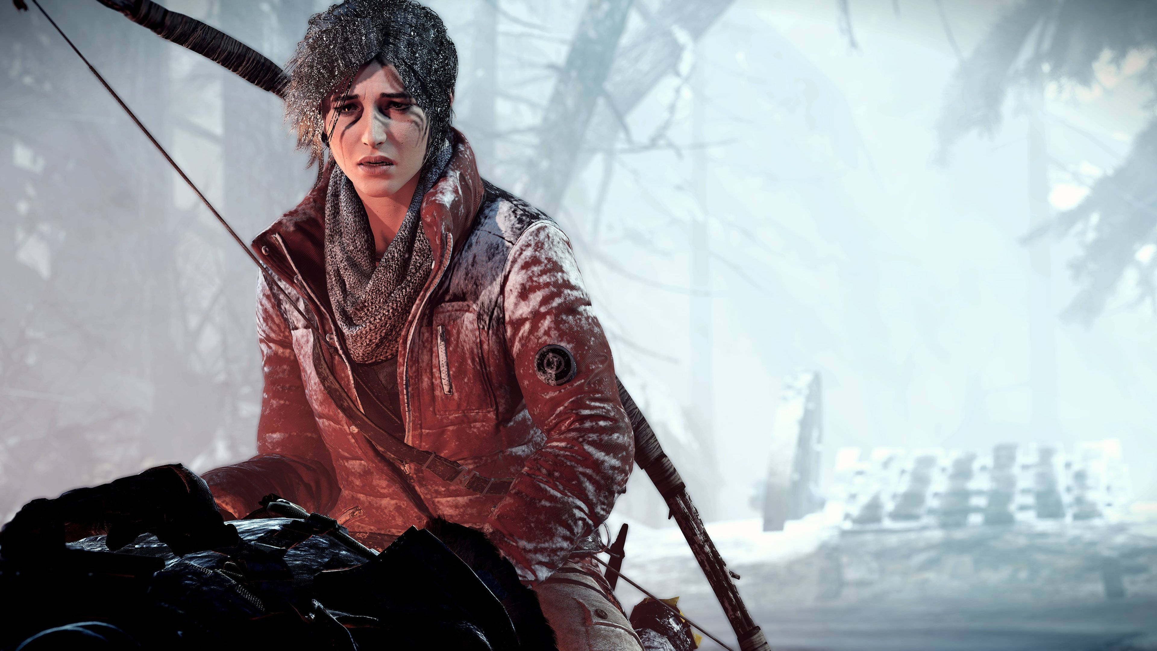 Lara Croft 桌布 壁紙 — 一位身穿紅色外套和毛帽、覆蓋著雪的弓箭手蹲伏在一個結霜的森林中，周圍有光禿禿的樹木和遠處的廢墟建築。