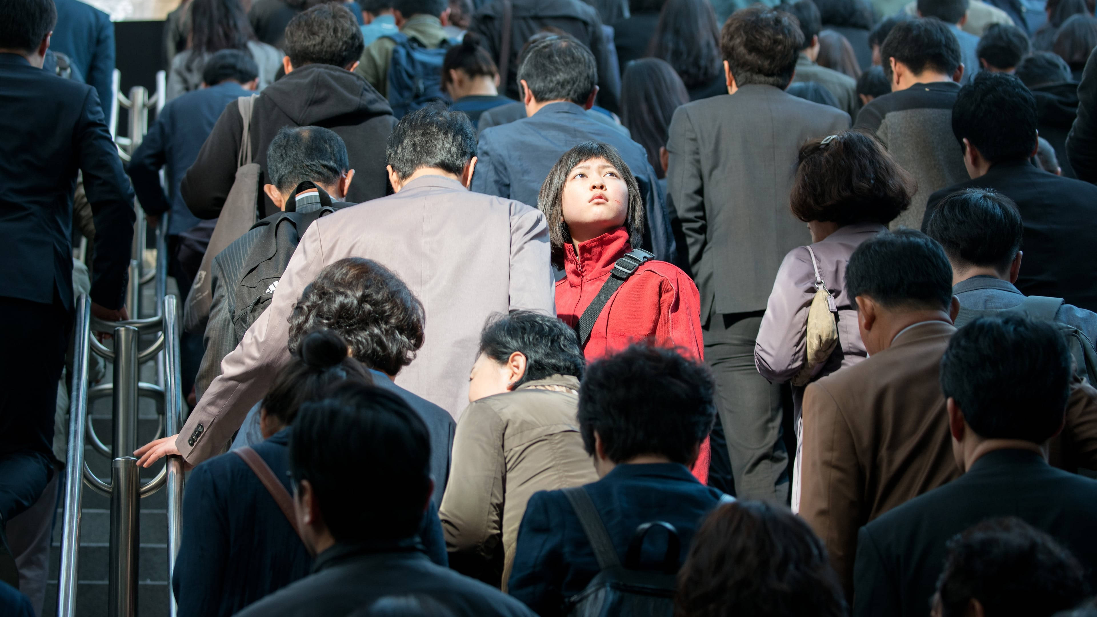 okja 桌布 壁紙 — 一位身穿紅色外套的年輕女子在擁擠的電梯人群中脫穎而出，他們正登上繁忙的自動扶梯。