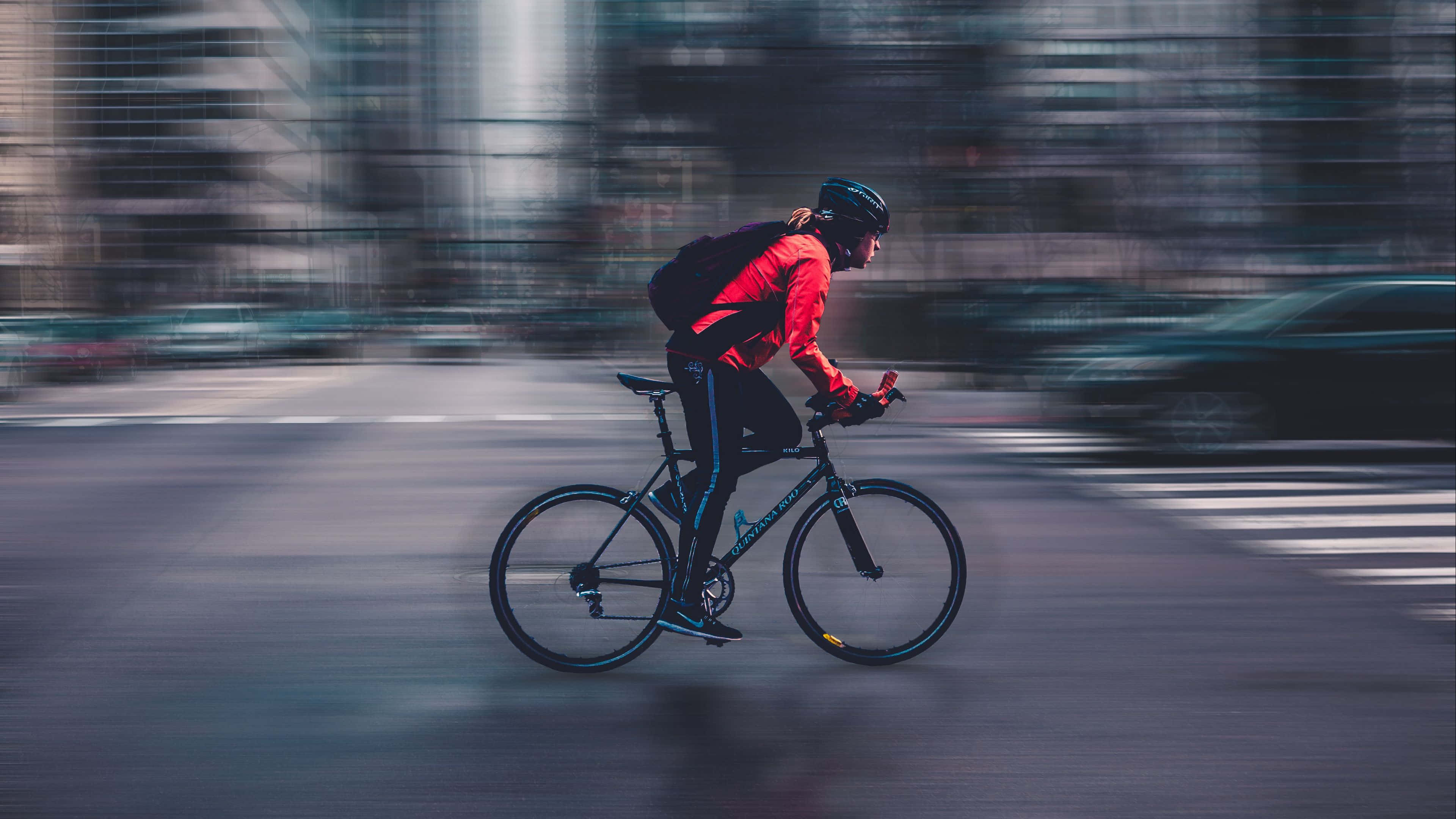 4K Bikes 桌布 壁紙 — 一位身穿紅色外套的自行車手在模糊的城市街道上快速踩踏，帶有動態條紋。