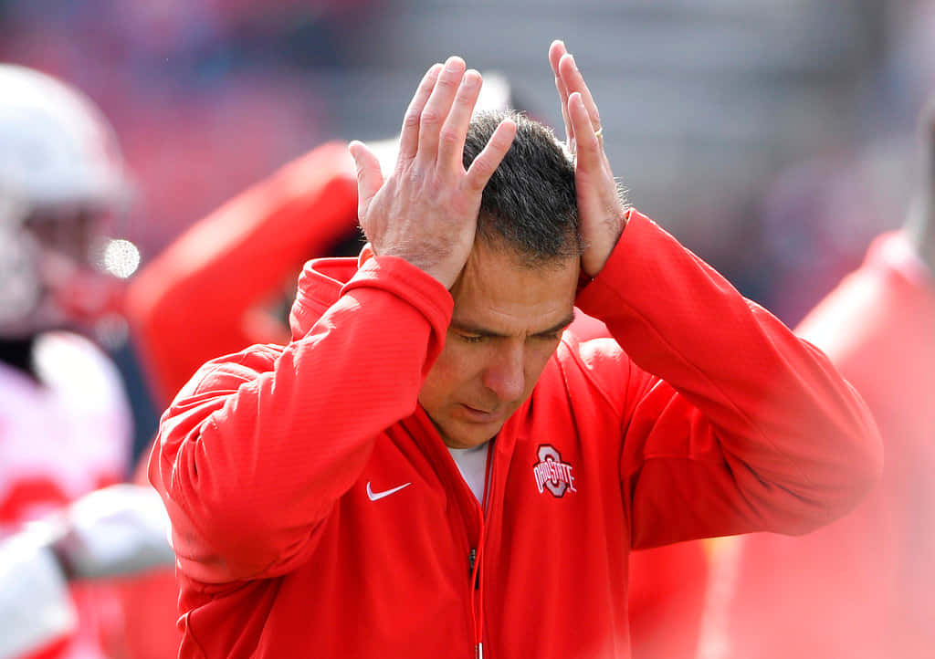Urban Meyer 桌布 壁紙 — 一位身穿紅色外套的足球教練在比賽中沮喪地抱住頭。