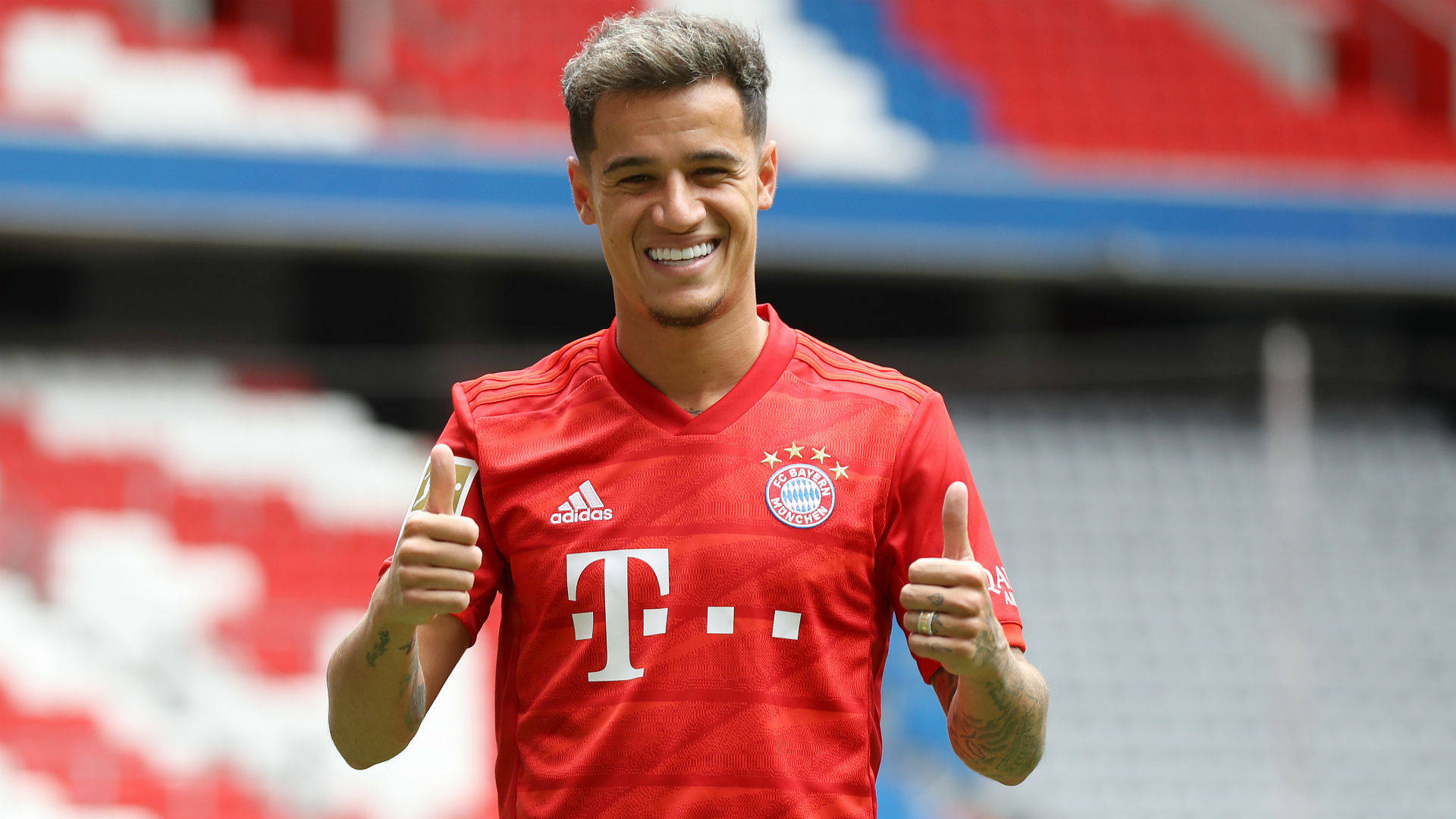 Coutinho 桌布 壁紙 — 一位身穿紅色拜仁慕尼黑球衣的足球員微笑著，在紅白相間座位的球場上豎起兩個大拇指。