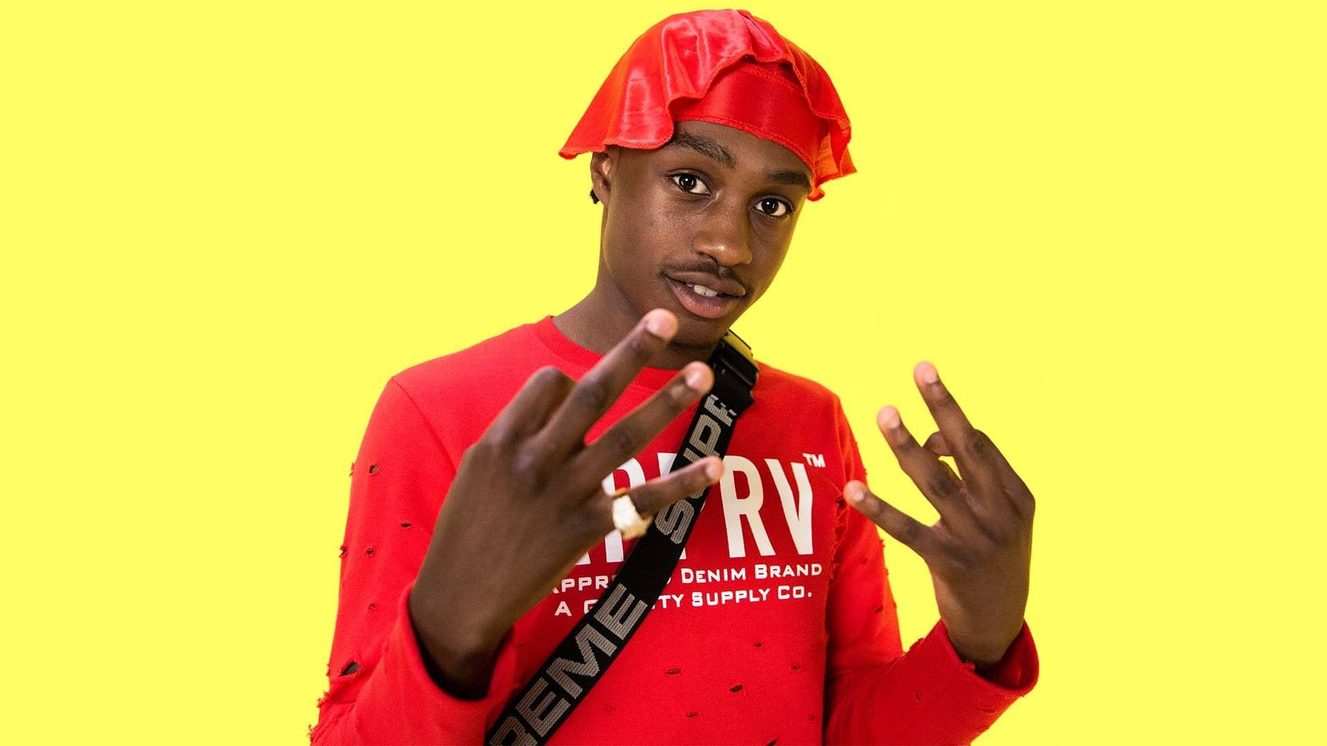 Lil Tjay 桌布 壁紙 — 一位身穿紅色服裝和帽子的年輕男子在亮黃色背景前做手勢。