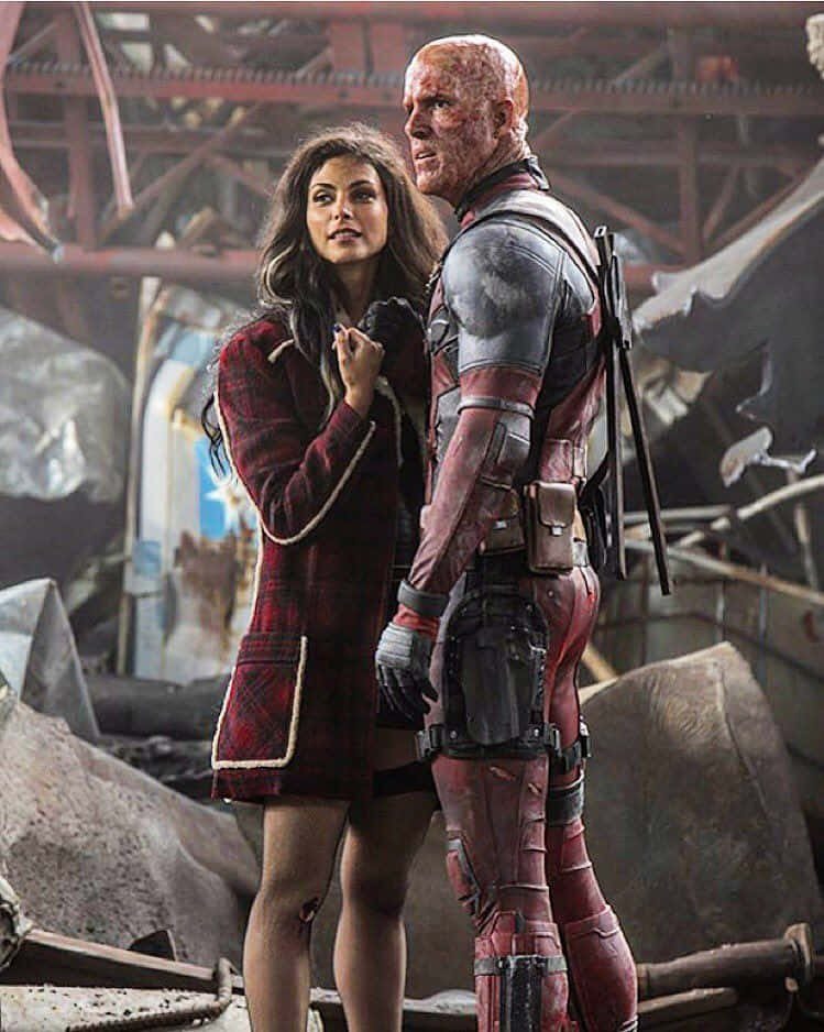 Deadpool And Vanessa 桌布 壁紙 — 一位身穿紅色格紋外套的女人站在一個血淋淋的死侍旁邊，背景是一個被破壞的工業環境。