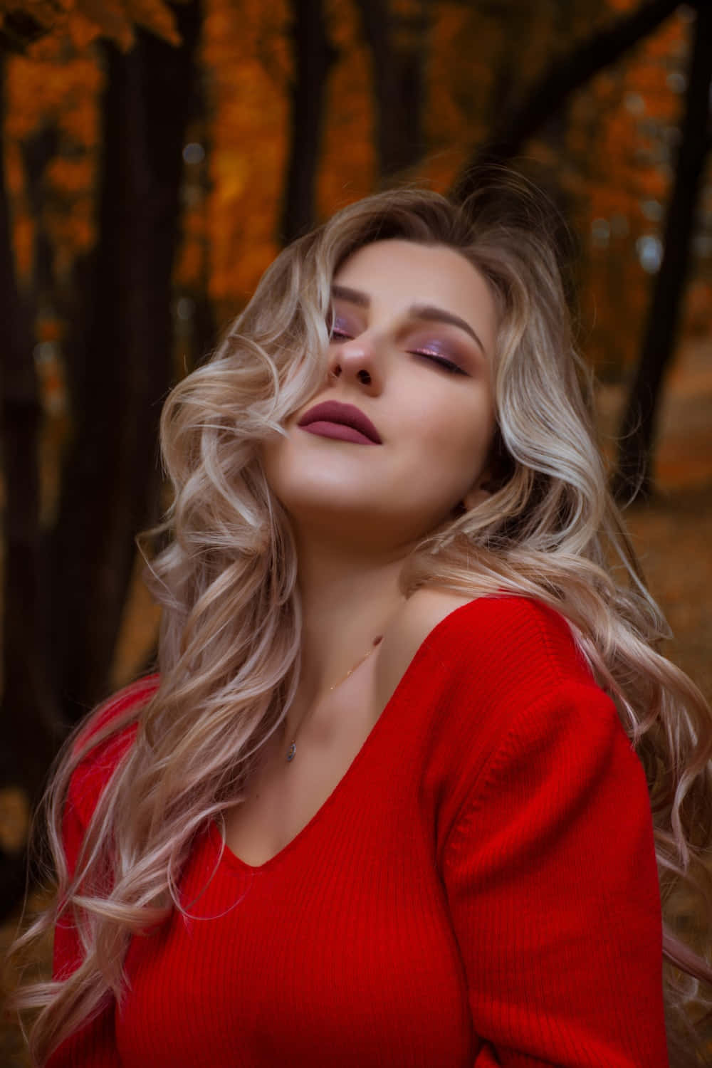 美女 桌布 壁紙 — 一位身穿紅色毛衣的女性在金色秋林中閉上眼睛，溫暖的陽光穿過樹木灑落。