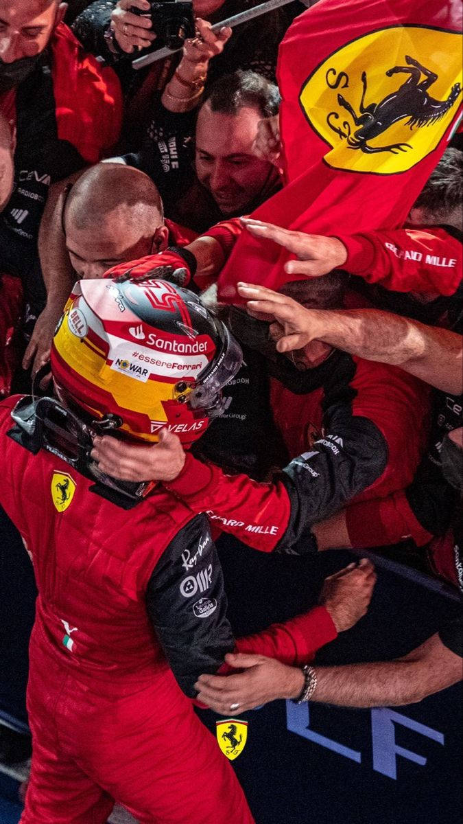 Racing 桌布 壁紙 — 一位身穿紅色法拉利裝備的一級方程式車手在比賽勝利後被團隊成員和手持法拉利旗幟的粉絲擁抱。
