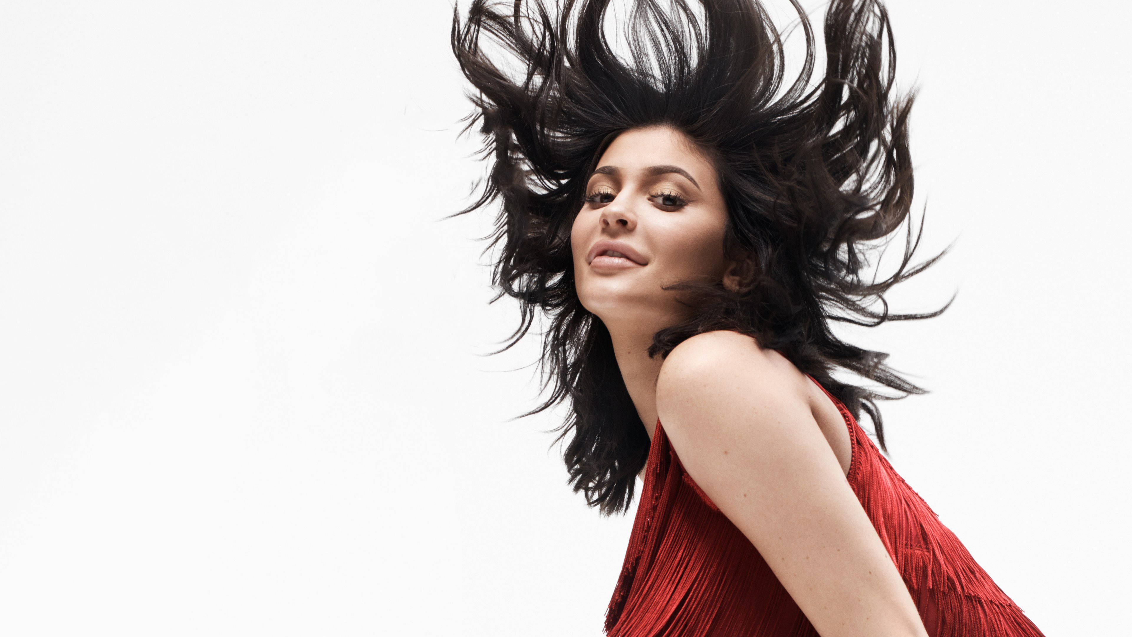 Kylie 桌布 壁紙 — 一位身穿紅色流蘇裙、黑色長髮飄逸的女性，在純白背景前動態飛揚。