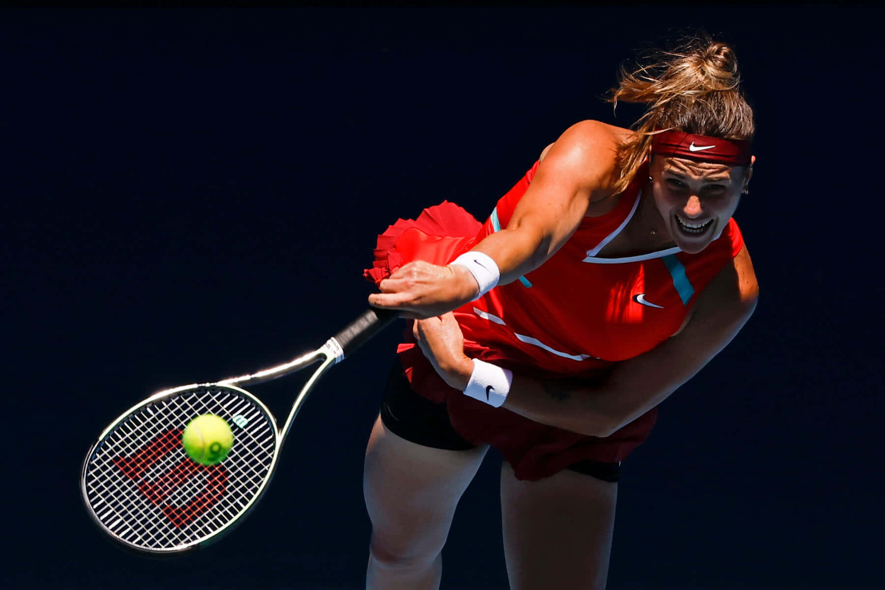 Athlete 桌布 壁紙 — 一位身穿紅色球衣的女網球運動員在深色背景下揮拍擊打一個亮黃色的球。