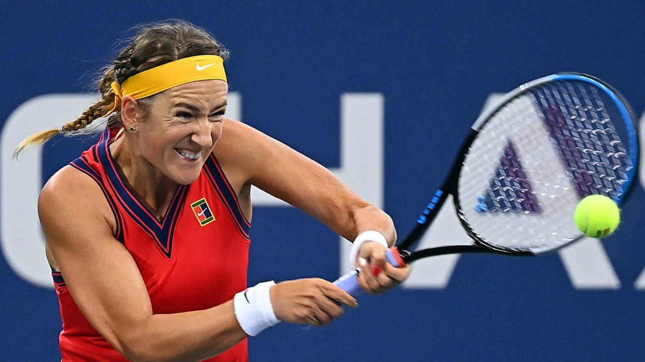 Athletic 桌布 壁紙 — 一位身穿紅色球衣的女網球選手在藍色球場背景下揮拍擊打一個亮黃色的網球。