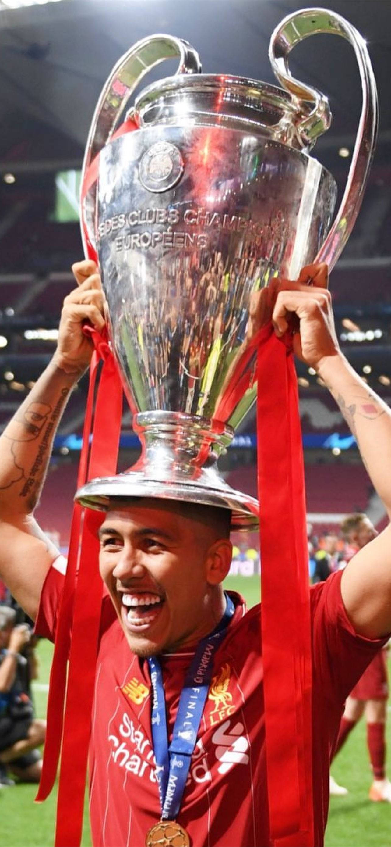 Champions League 桌布 壁紙 — 一位身穿紅色球衣的快樂足球運動員在球場上將閃閃發光的歐冠獎盃高舉過頭頂。