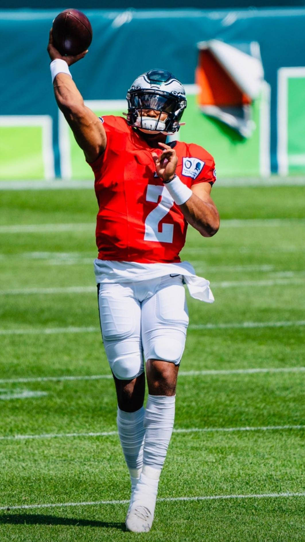 Jalen Hurts Eagles 桌布 壁紙 — 一位身穿紅色球衣的美式足球四分衛在晴朗的白天於明亮的綠色球場上傳球。