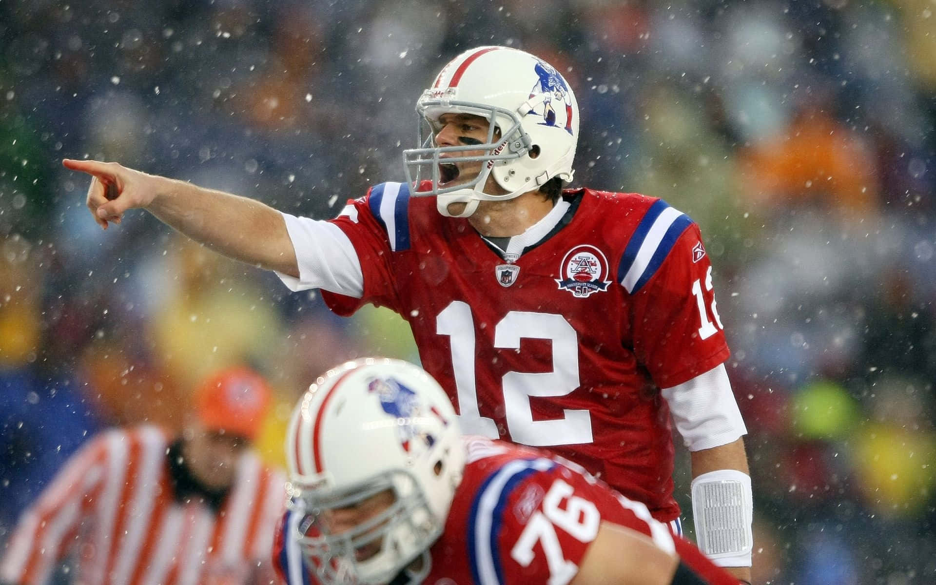 Patriots 桌布 壁紙 — 一位身穿紅色球衣的美式足球四分衛在雪地比賽中向前指，前景有隊友。