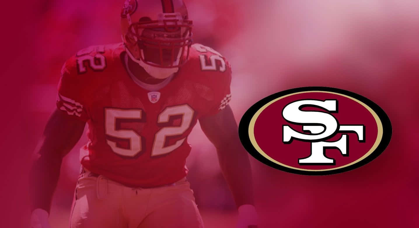 49ers 桌布 壁紙 — 一位身穿紅色球衣號碼52的舊金山49人美式足球員站在煙霧瀰漫的粉紅燈光下，旁邊是球隊標誌。