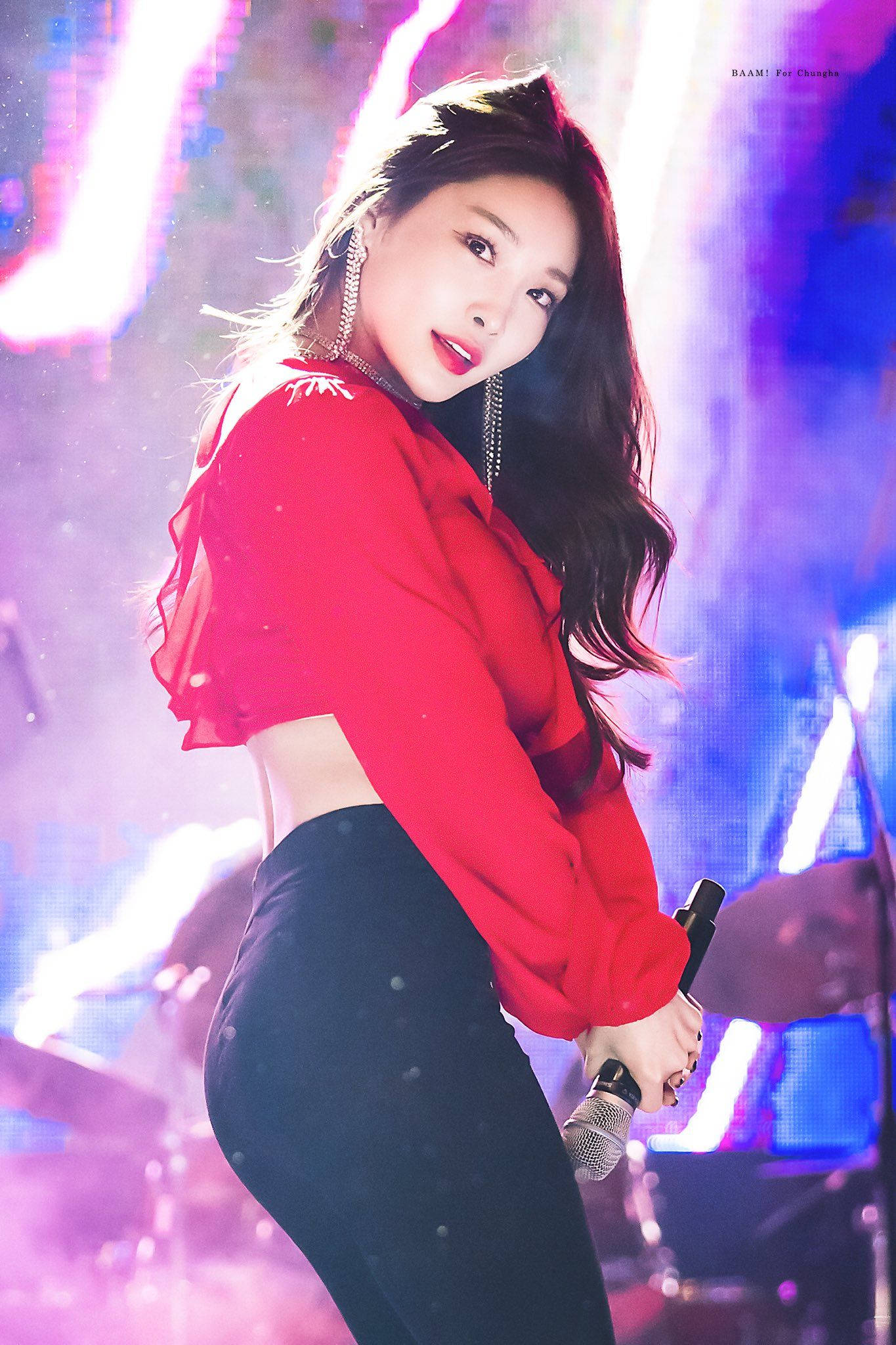 Chungha 桌布 壁紙 — 一位身穿紅色短上衣和黑色褲子的女表演者在充滿活力的紫色和藍色舞台燈光下拿著麥克風。