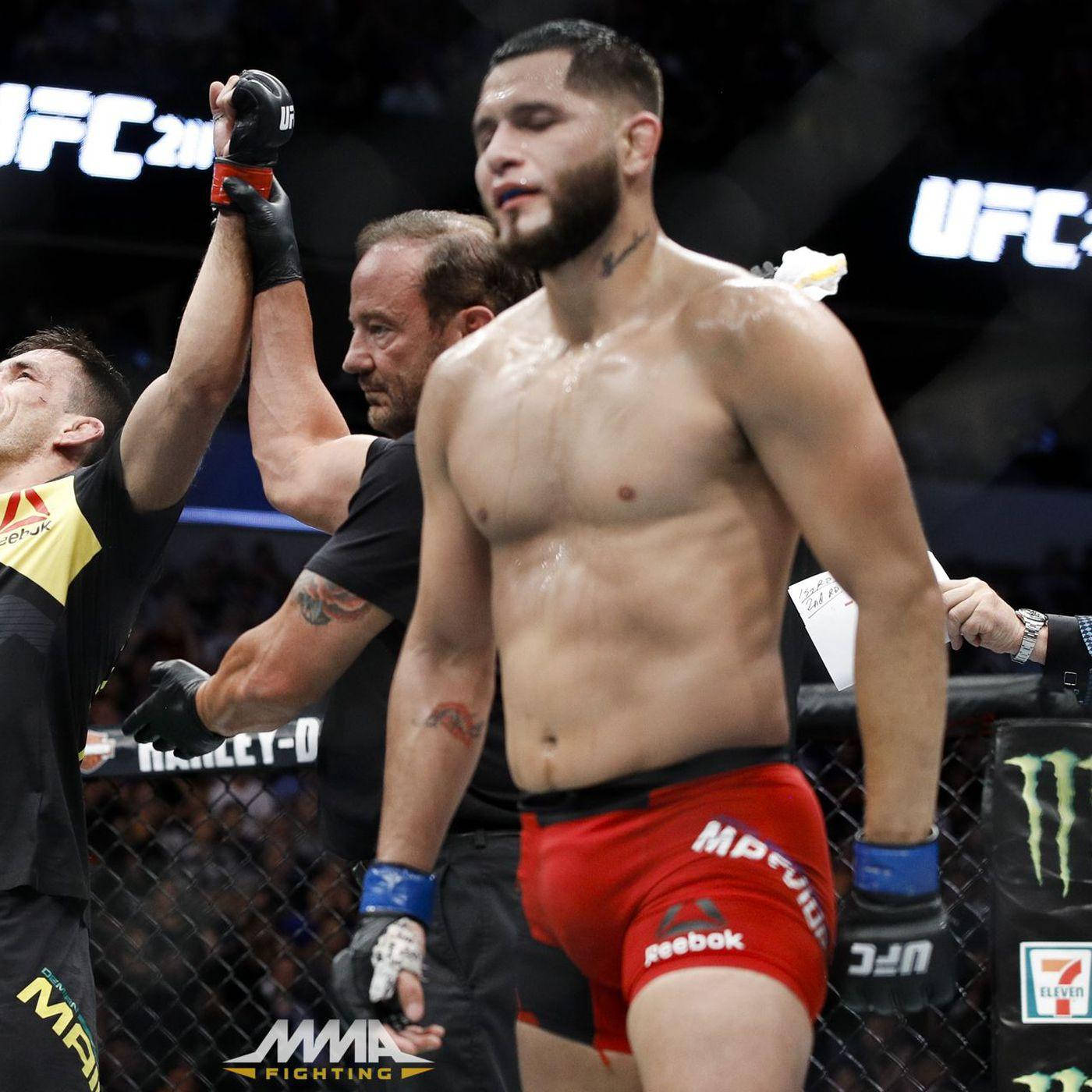 UFC 桌布 壁紙 — 一位身穿紅色短褲的UFC勝利者站在八角籠中，裁判在明亮的場館燈光下高舉他的手以示勝利。