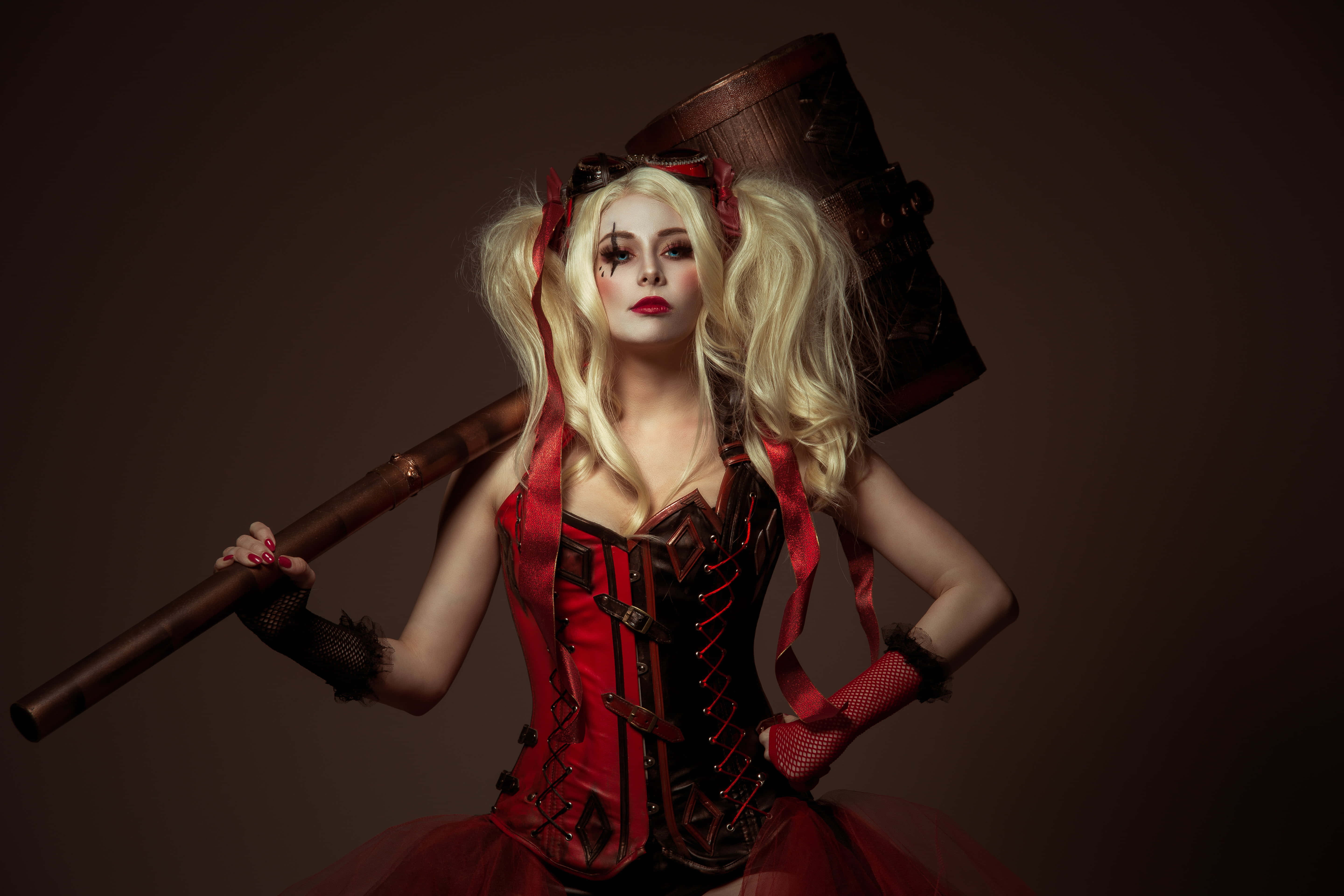 Harley Quinn Hammer 桌布 壁紙 — 一位身穿紅色緊身胸衣和雙馬尾的女性，在深棕色背景前手持一把大槌。