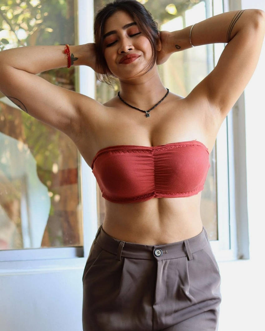 hot babes 桌布 壁紙 — 一位身穿紅色羅紋掛頸上衣和灰色長褲的女性站在窗邊，雙臂高舉，閉著眼睛，露出平靜的微笑。