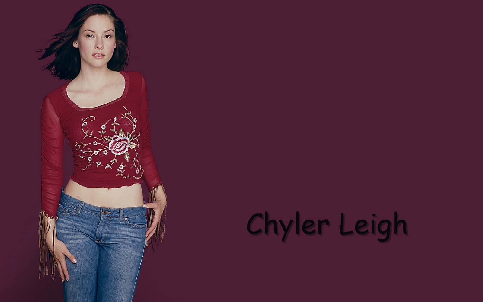 Chyler Leigh 桌布 壁紙 — 一位身穿紅色花卉上衣和牛仔褲的女性站在深栗色背景前，附近寫有她的名字。