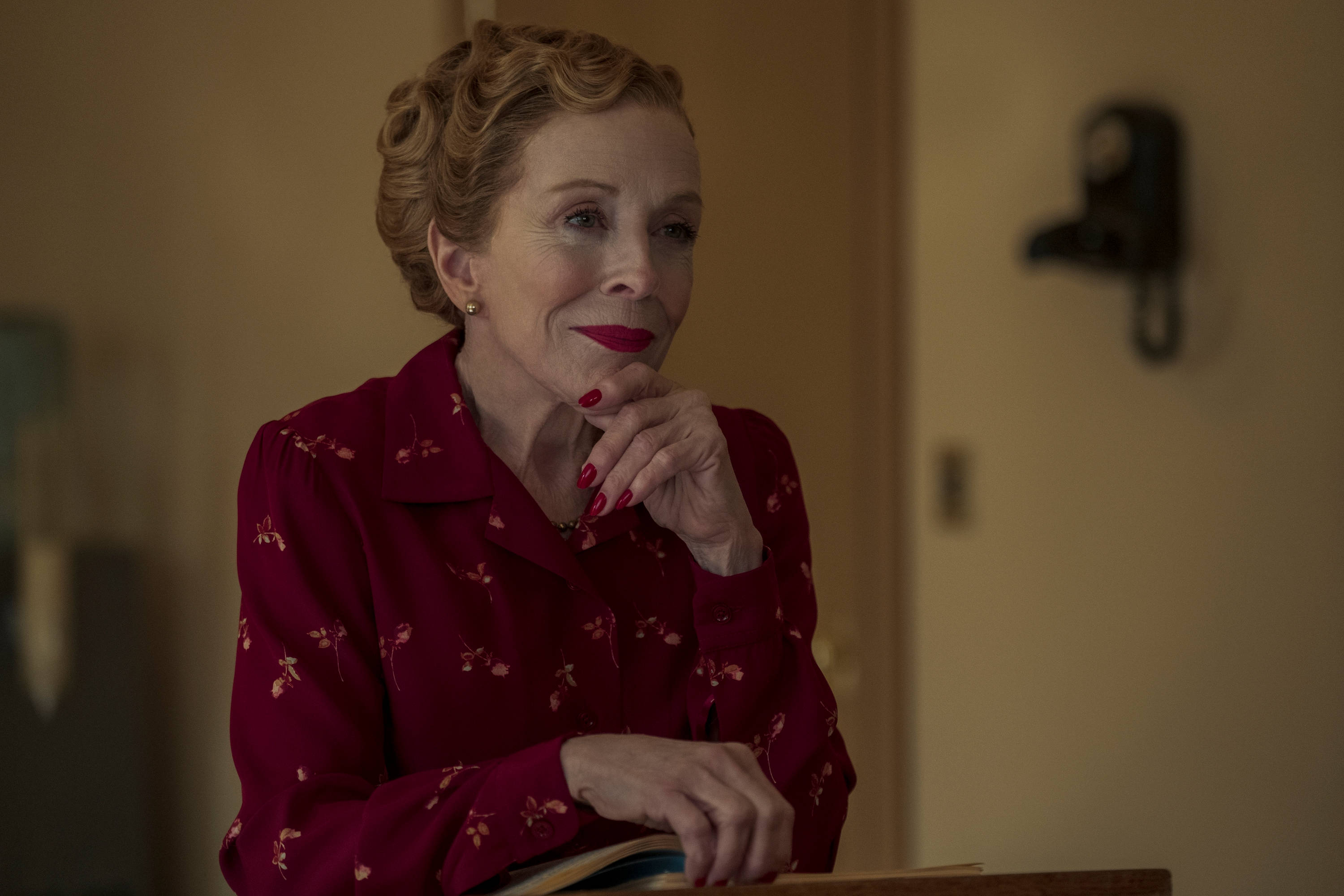 Netflix 桌布 壁紙 — 一位身穿紅色花卉圖案襯衫的女性，在溫暖光線的房間裡，用手托著下巴，表情若有所思。