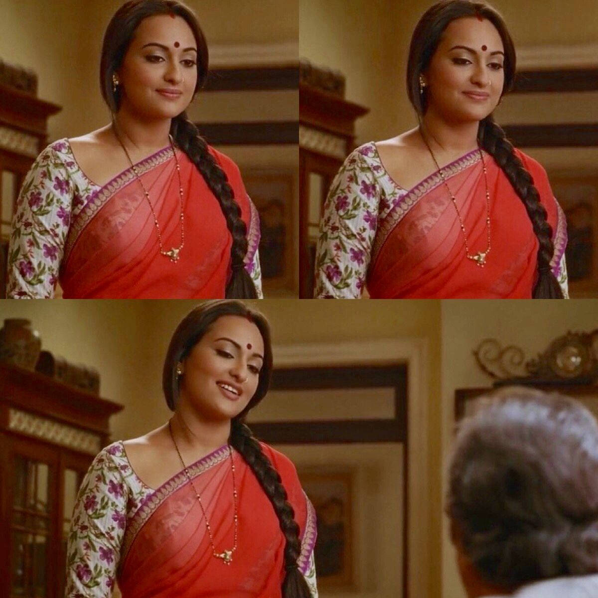 Sonakshi Sinha 桌布 壁紙 — 一位身穿紅色花卉紗麗的女性在室內與一位年長者交談時溫暖地微笑。