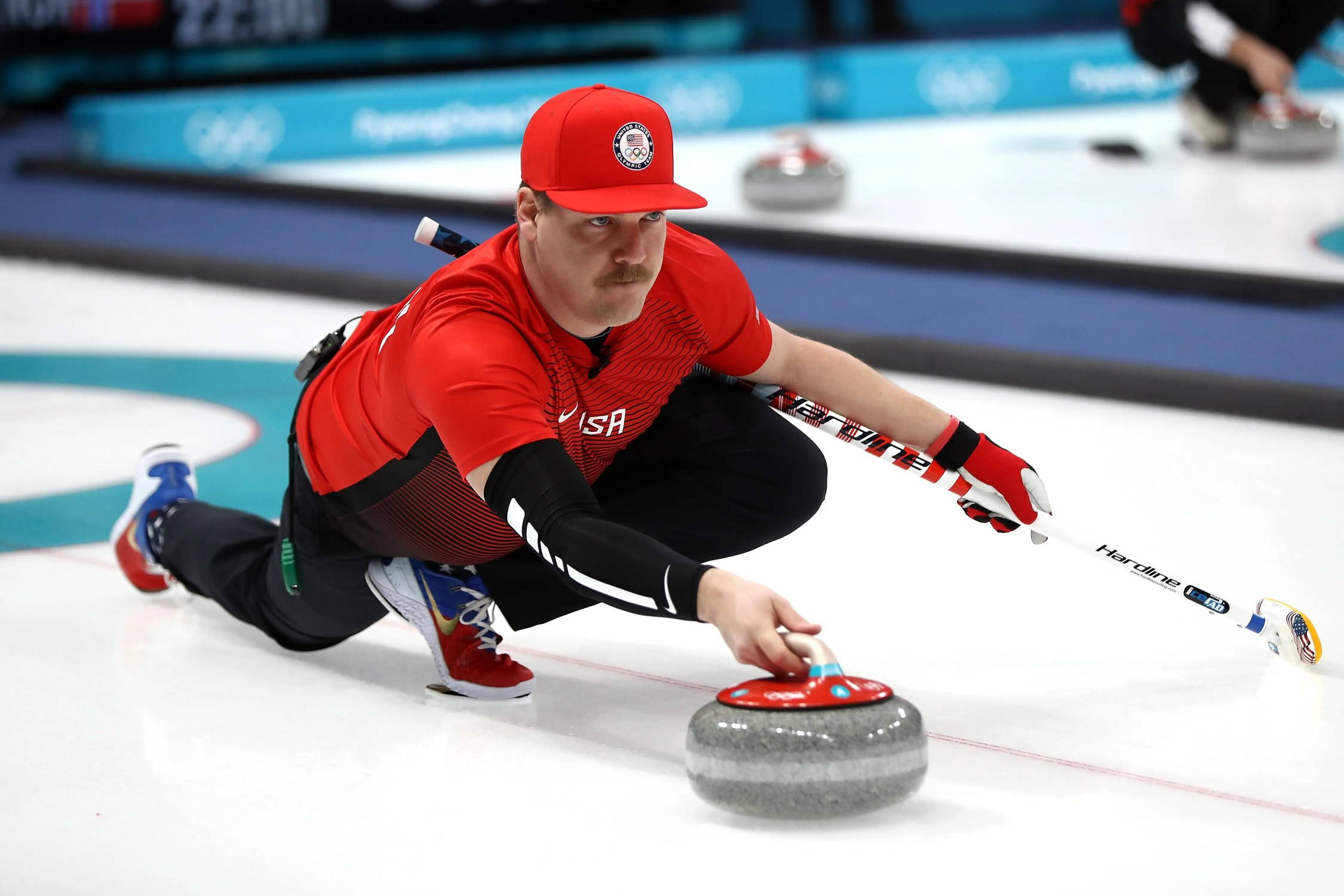 Olympics 桌布 壁紙 — 一位身穿紅色裝備、專注的美國冰壺選手在奧運比賽中將花崗岩冰壺石在冰上滑行。
