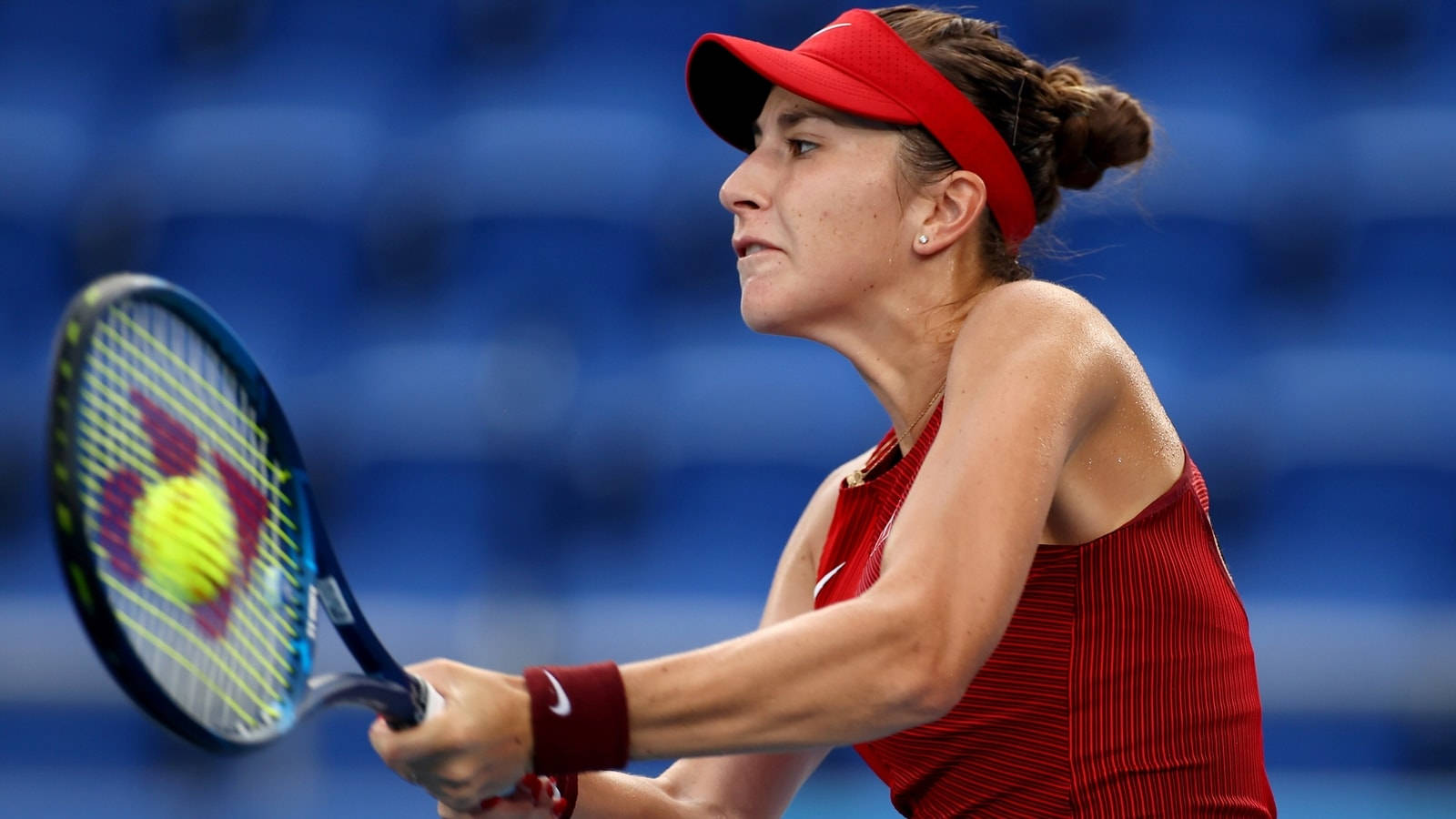 Athletic 桌布 壁紙 — 一位身穿紅色裝備的女網球選手在模糊的藍色體育場背景下揮拍擊打黃色球。