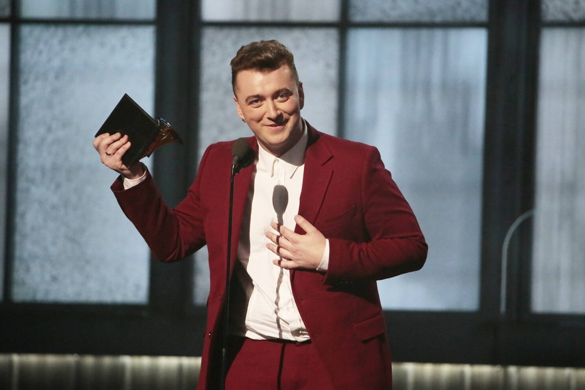 Sam Smith 桌布 壁紙 — 一位身穿紅色西裝、面帶微笑的男子站在舞台上的麥克風前，高舉葛萊美獎。